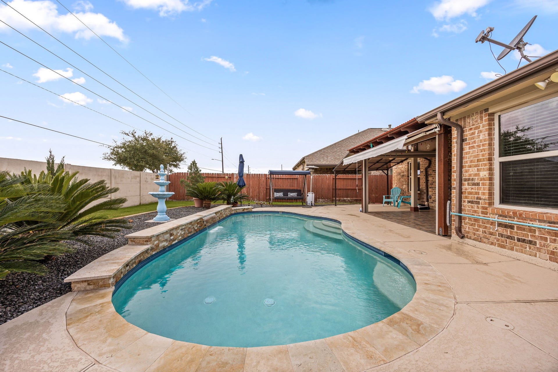 Your private backyard resort! This stunning, crystal-clear in-ground pool features a flagstone coping border, a raised stone water feature wall, entry steps, and a tiered rock waterfall/fountain display.