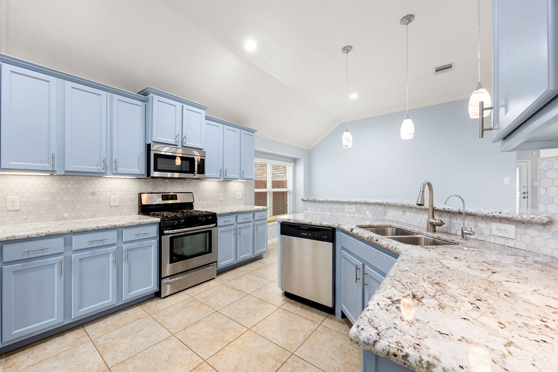 A beautiful view of the updated kitchen, complete with striking granite surfaces, ample cabinet storage, stylish pendant light fixtures over the bar, and a vaulted ceiling with recessed lights.