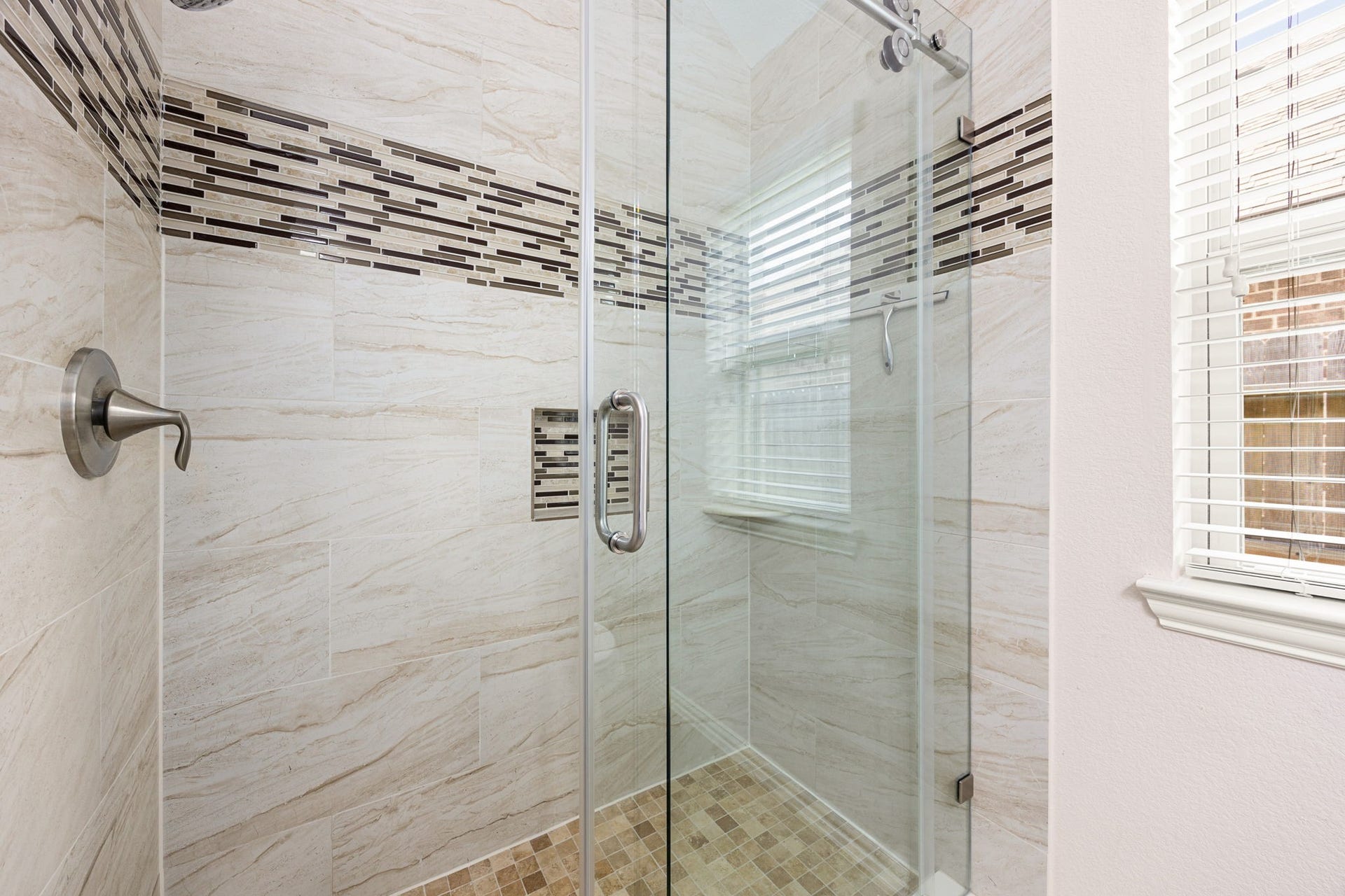 The secondary bathroom boasts a premium walk-in shower finished with elegant floor-to-ceiling tile work, a decorative mosaic accent band, a built-in shampoo niche, and a sleek frameless sliding glass door.