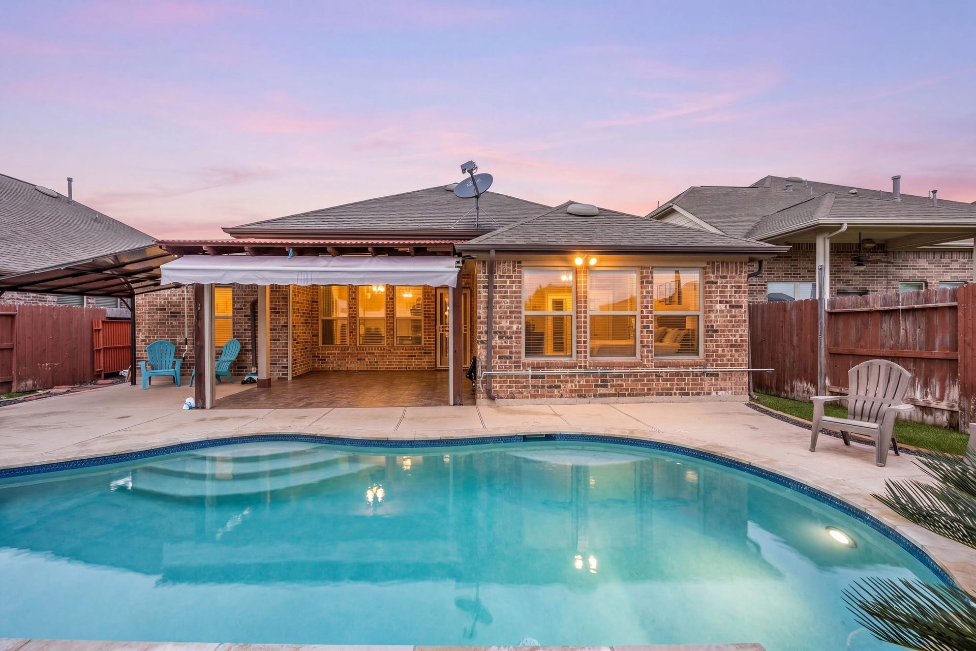 This stunning perspective highlights the expansive clear pool, premium brick home construction, extensive concrete decking, and wide covered patio layout built for endless outdoor enjoyment.