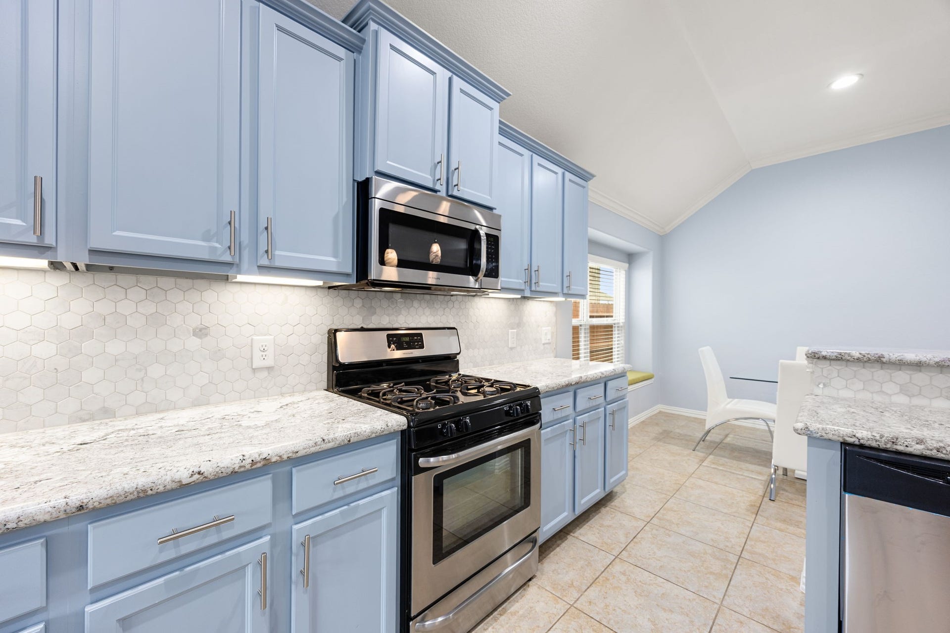 Fully equipped with premium stainless steel appliances, including a gas range and built-in microwave, beautifully complementing the granite countertops and honeycomb tile backsplash.