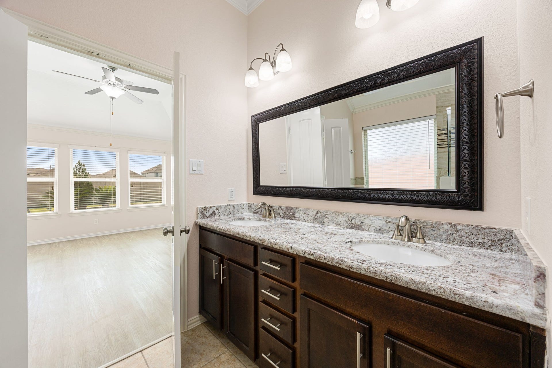 The primary bathroom features an expansive double-sink vanity topped with premium granite countertops, rich dark cabinetry with modern t-bar hardware, and an oversized decorative framed mirror.