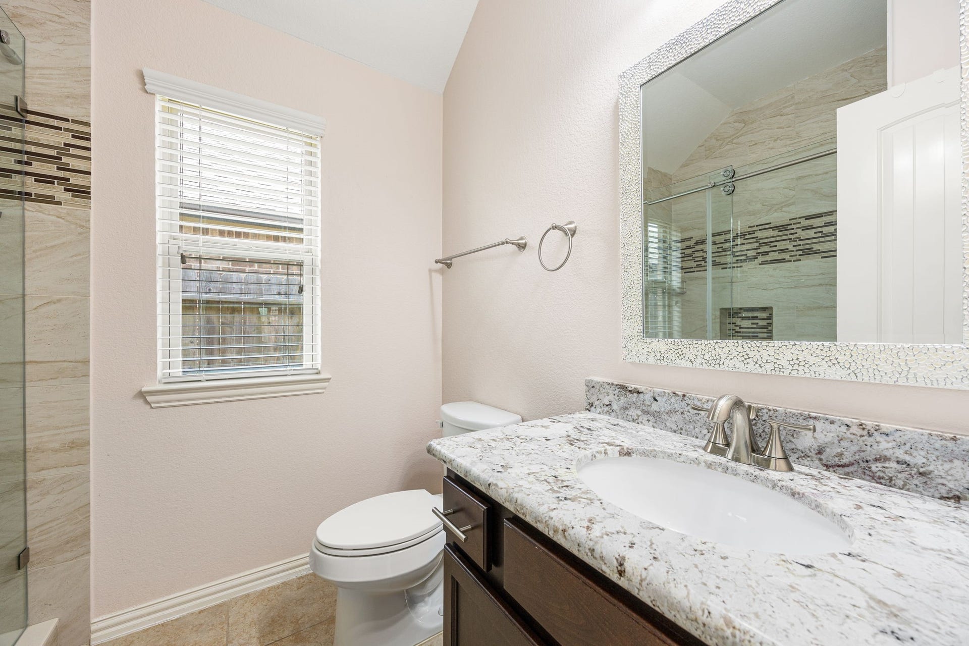 Beautifully updated secondary bathroom featuring a premium granite vanity countertop, an oversized decorative mirror, tile flooring, and a window that lets in soft natural light.