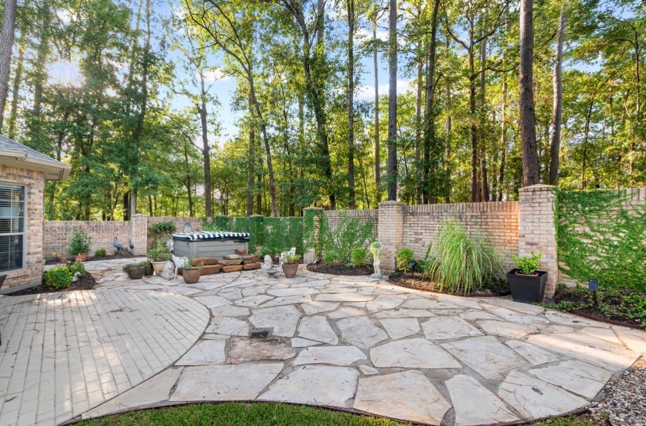 901 Longmire Road, #51, Conroe, TX 77304 A beautifully secluded backyard oasis featuring an expansive natural stone patio, lush landscaping, a privacy wall & a hardwired Jacuzzi, surrounded by majestic trees for the ultimate outdoor retreat.