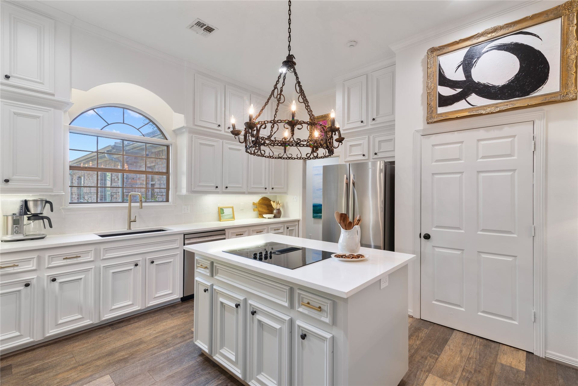 901 Longmire Road, #51, Conroe, TX 77304 A beautifully appointed kitchen featuring crisp white cabinetry, a spacious center island, elegant chandelier, arched window & abundant natural light. A perfect blend of timeless charm and modern sophistication.