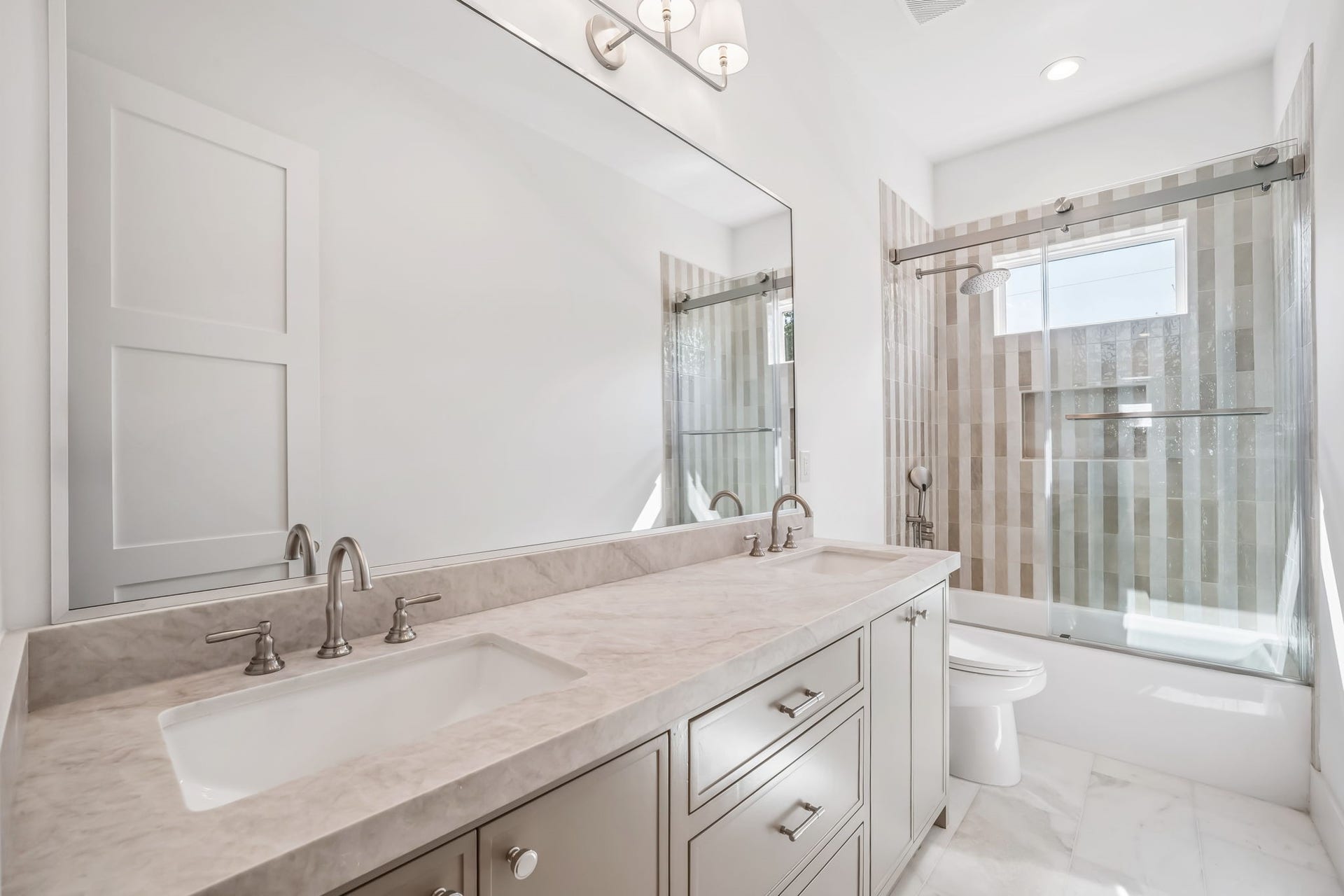 Second-floor hall bath featuring dual sinks, an enclosed shower/tub combination, and marble flooring.