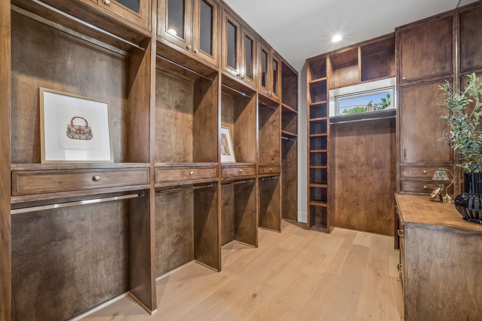 Luxurious custom walk-in closet featuring rich wood cabinetry, built-in shelving, dedicated hanging space, and elegant drawer storage with warm hardwood flooring.