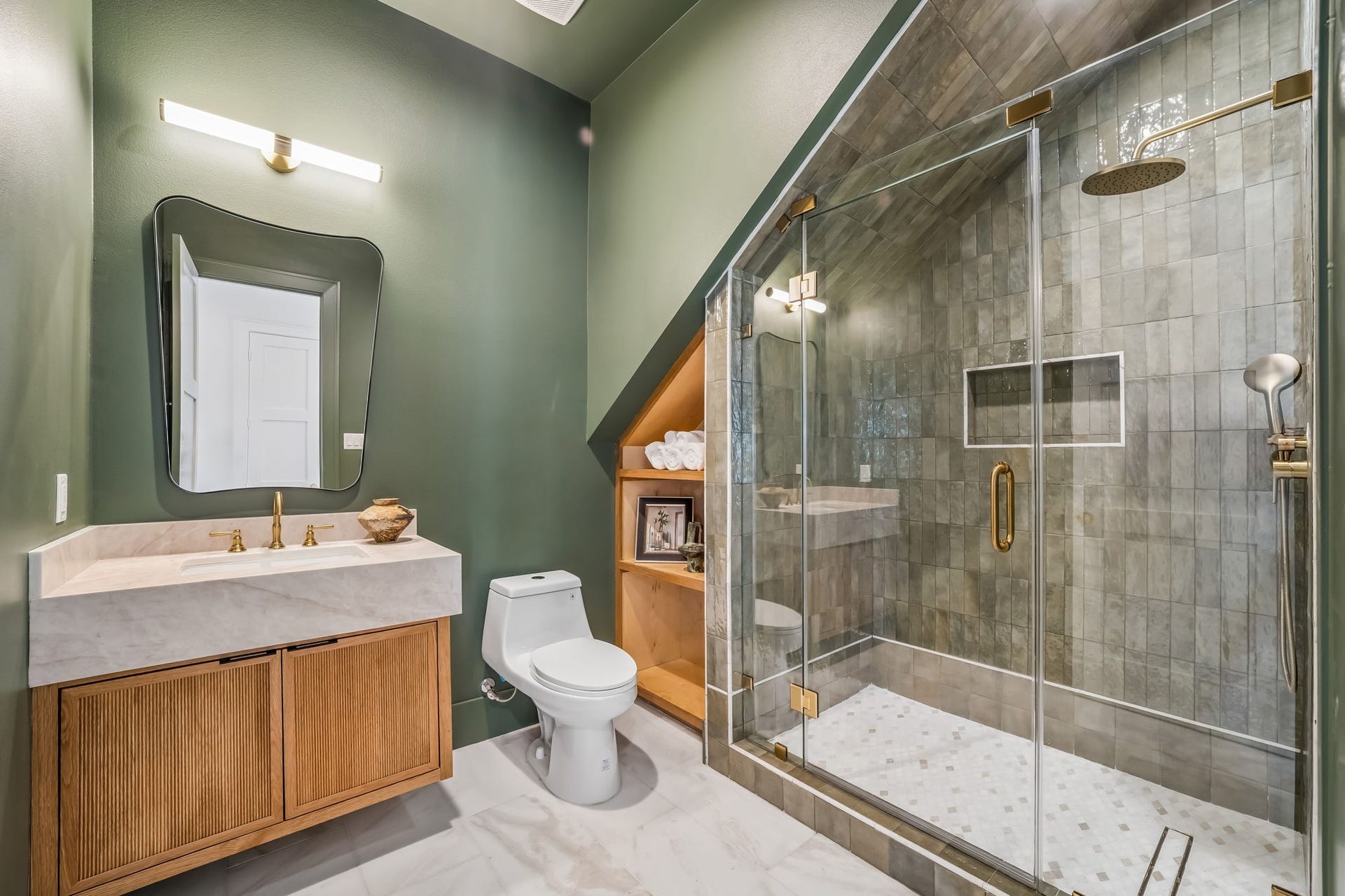 The downstairs guest bath makes a statement with a floating vanity accented by reeded white oak, marble flooring, and a rich, earthy green color-drench across the walls and ceiling for a sophisticated finish.