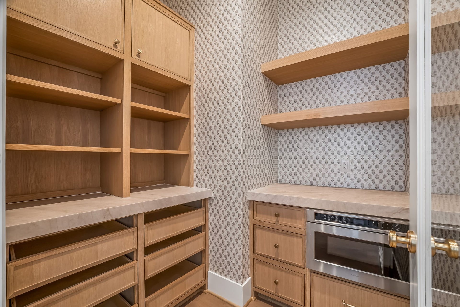 The walk-in pantry is thoughtfully designed with a built-in microwave and a mix of open and closed storage, keeping everyday essentials beautifully organized and within reach. Phillip Jeffries wallpaper adds the perfect decorative touch, making even this space feel elevated and intentional.
