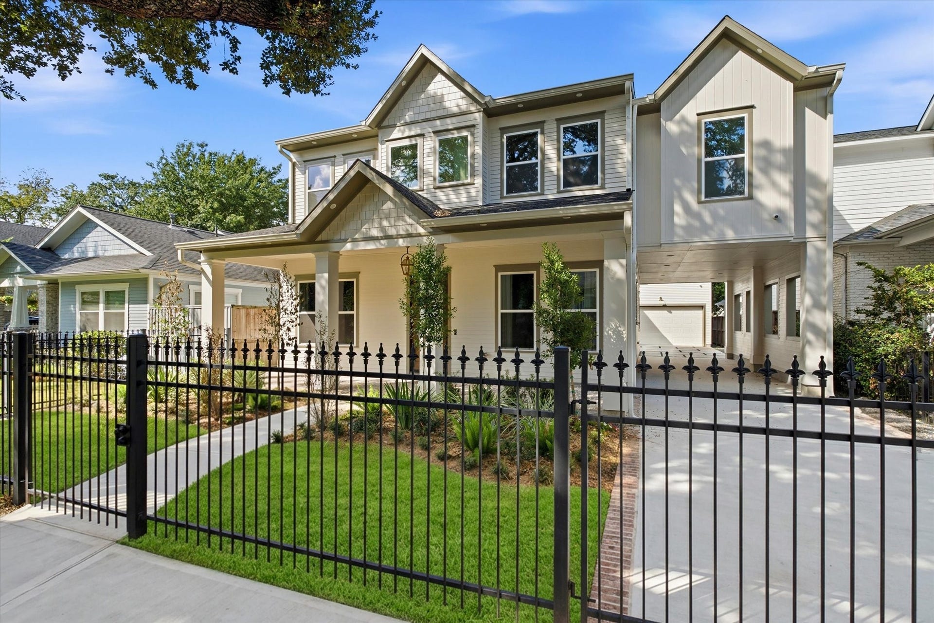A beautifully designed two-story home featuring an inviting covered front porch, manicured landscaping, elegant black iron fencing, and a spacious driveway, all complemented by timeless architectural finishes.