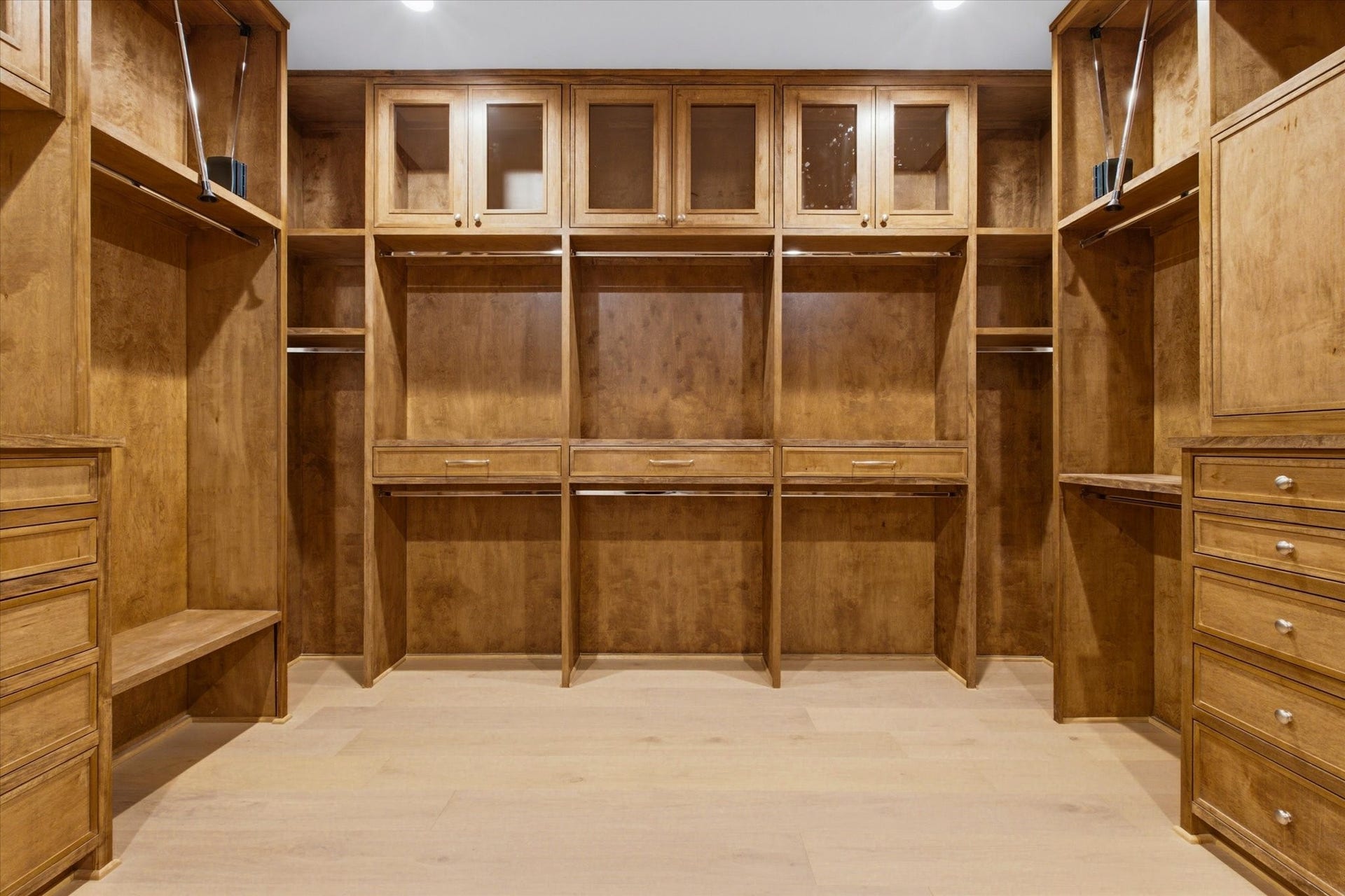 A showstopping, fully custom primary closet designed with every detail in mind, featuring pull-down third-tier hanging, under-cabinet lighting, glass-enclosed storage, and prewiring for the statement chandelier of your dreams.