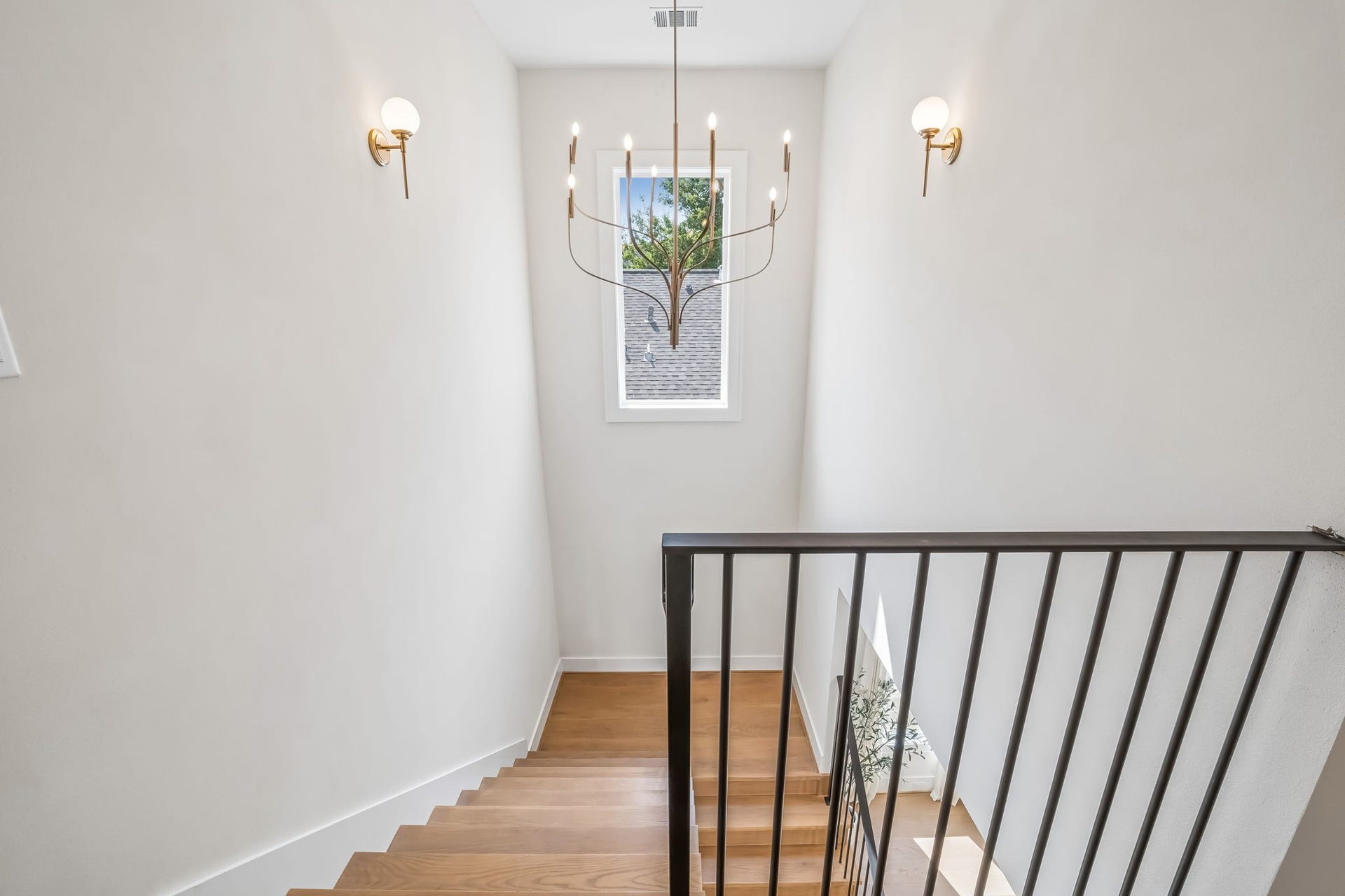 The stucco-finished landing is beautifully accented by Kichler lighting, white oak flooring, and a custom iron handrail, bringing warmth, texture, and architectural detail to the transition between floors 1 and 2.