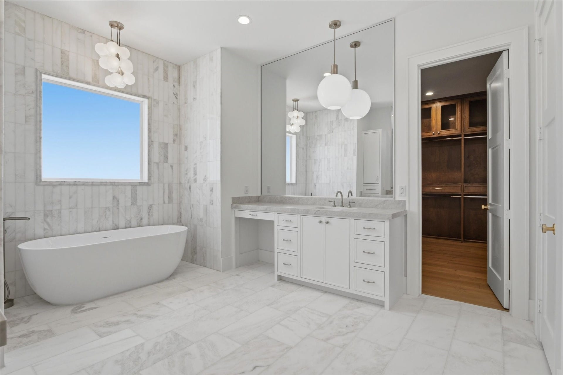 En-suite primary bath featuring marble flooring, Visual Comfort pendant lighting, a freestanding soaking tub, and separate vanities for a refined, spa-like retreat.