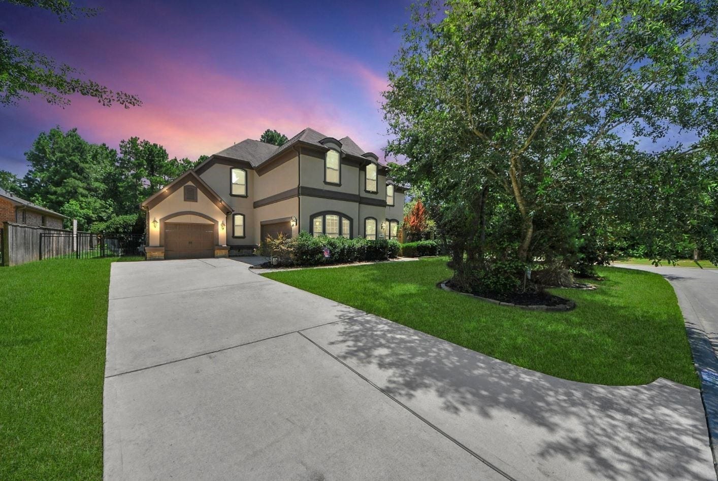 This striking corner-lot residence glows at dusk, with warm light spilling from sconces and windows onto a manicured lawn and smooth driveway. The blend of stone, stucco, and brick offers a rich contrast against the twilight sky.