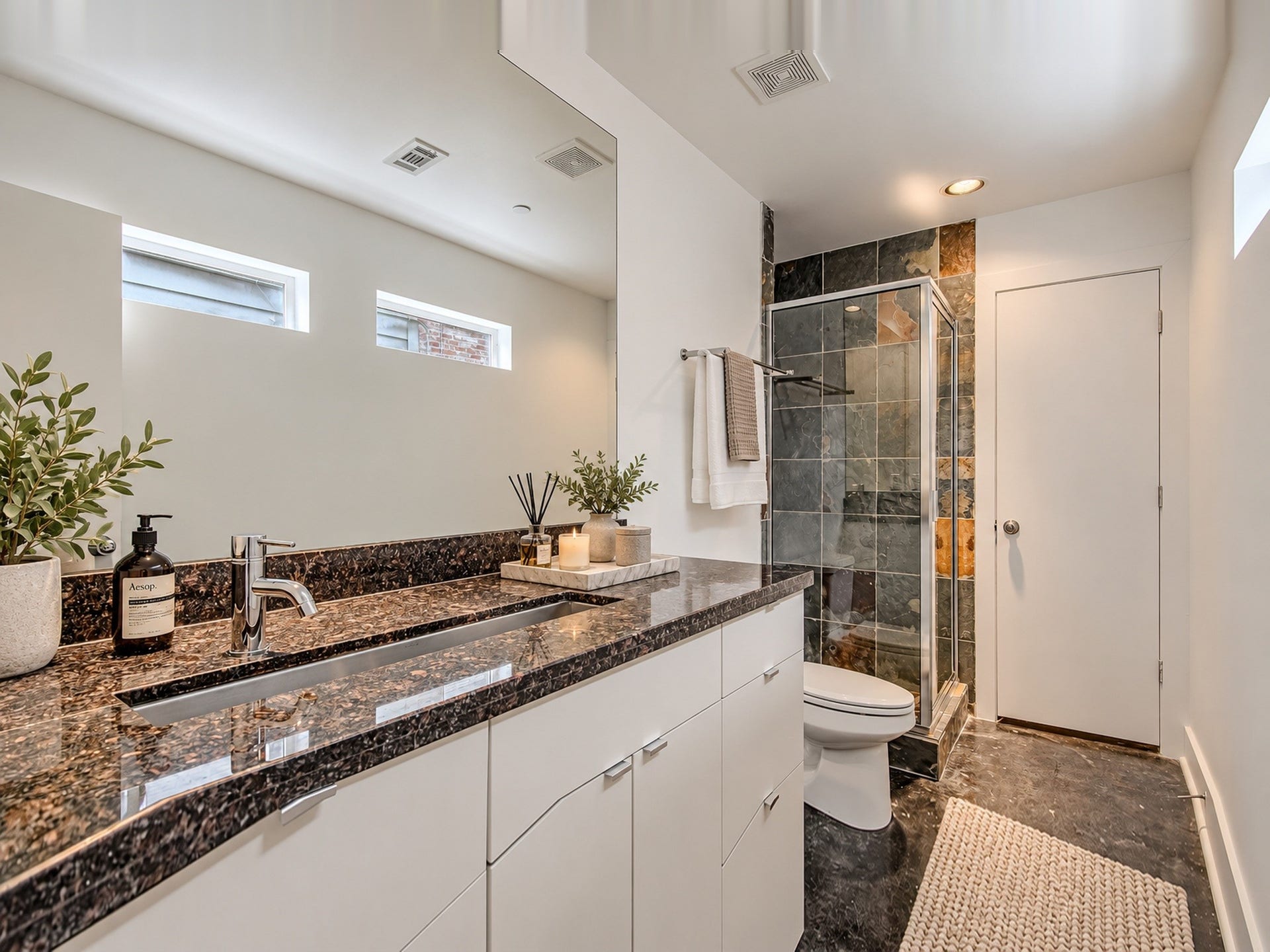 2025 Colquitt Street, #E, Houston, TX 77098 Bathroom vanity with an extended countertop, white cabinetry, high windows, and an adjacent glass-enclosed shower.