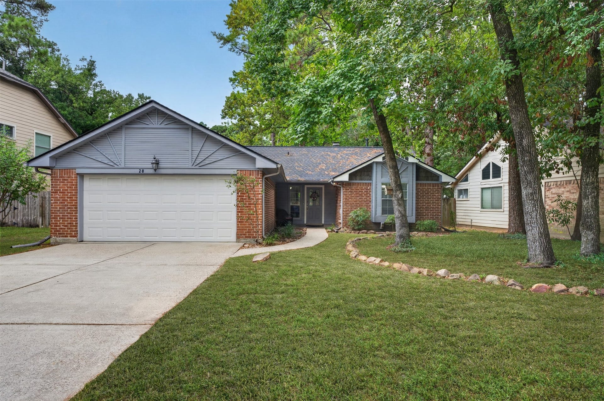28 S Rain Forest Court, The Woodlands, TX 77380 Charming brick home with a spacious two-car garage and a welcoming driveway, nestled among mature trees for added privacy and tranquility.