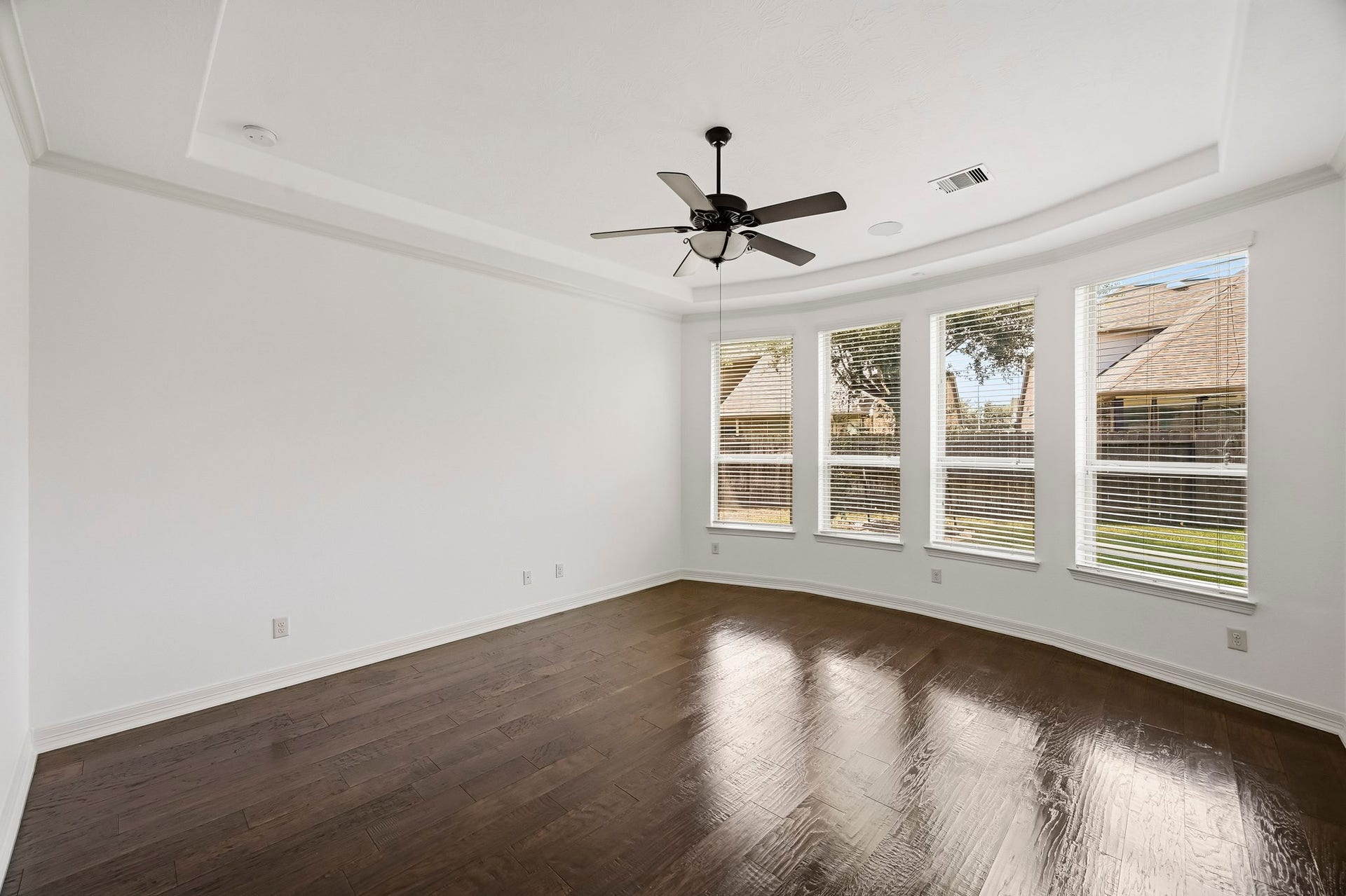 27730 Dalton Bluff Court, Katy, TX 77494 This spacious primary bedroom features rich wood flooring, neutral finishes, and an elegant tray ceiling with crown molding. A wall of four large windows fills the room with abundant natural light, while the generous layout provides plenty of space for a king-size bed, additional seating, and bedroom furnishings. A ceiling fan with integrated lighting completes this bright and inviting primary retreat.
