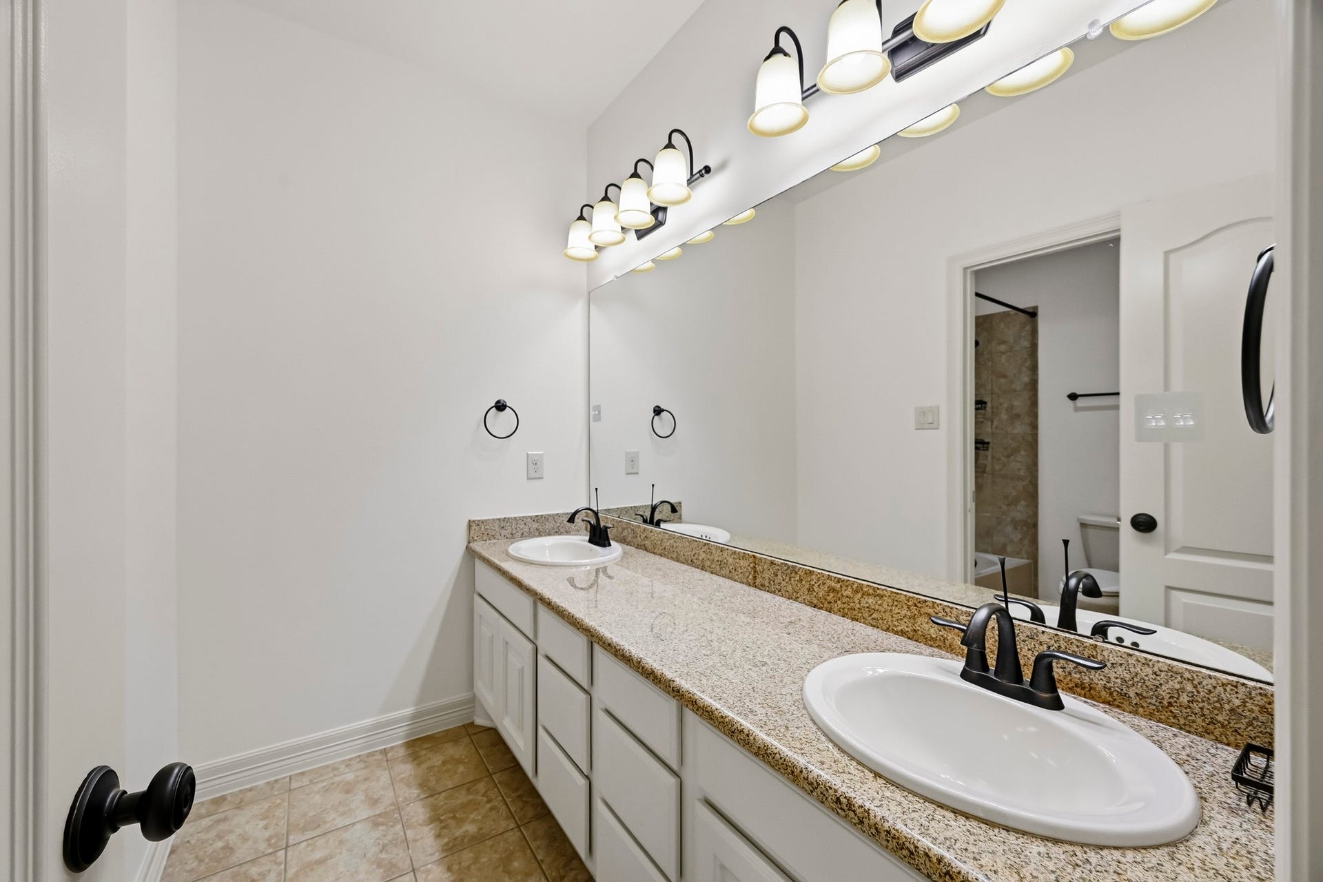 27730 Dalton Bluff Court, Katy, TX 77494 This spacious bathroom vanity features dual sinks set in a long granite countertop with ample cabinetry and drawer storage below. An expansive wall-to-wall mirror and multiple vanity lights brighten the space, while dark fixtures provide contrast against the crisp white cabinetry and neutral tile flooring.