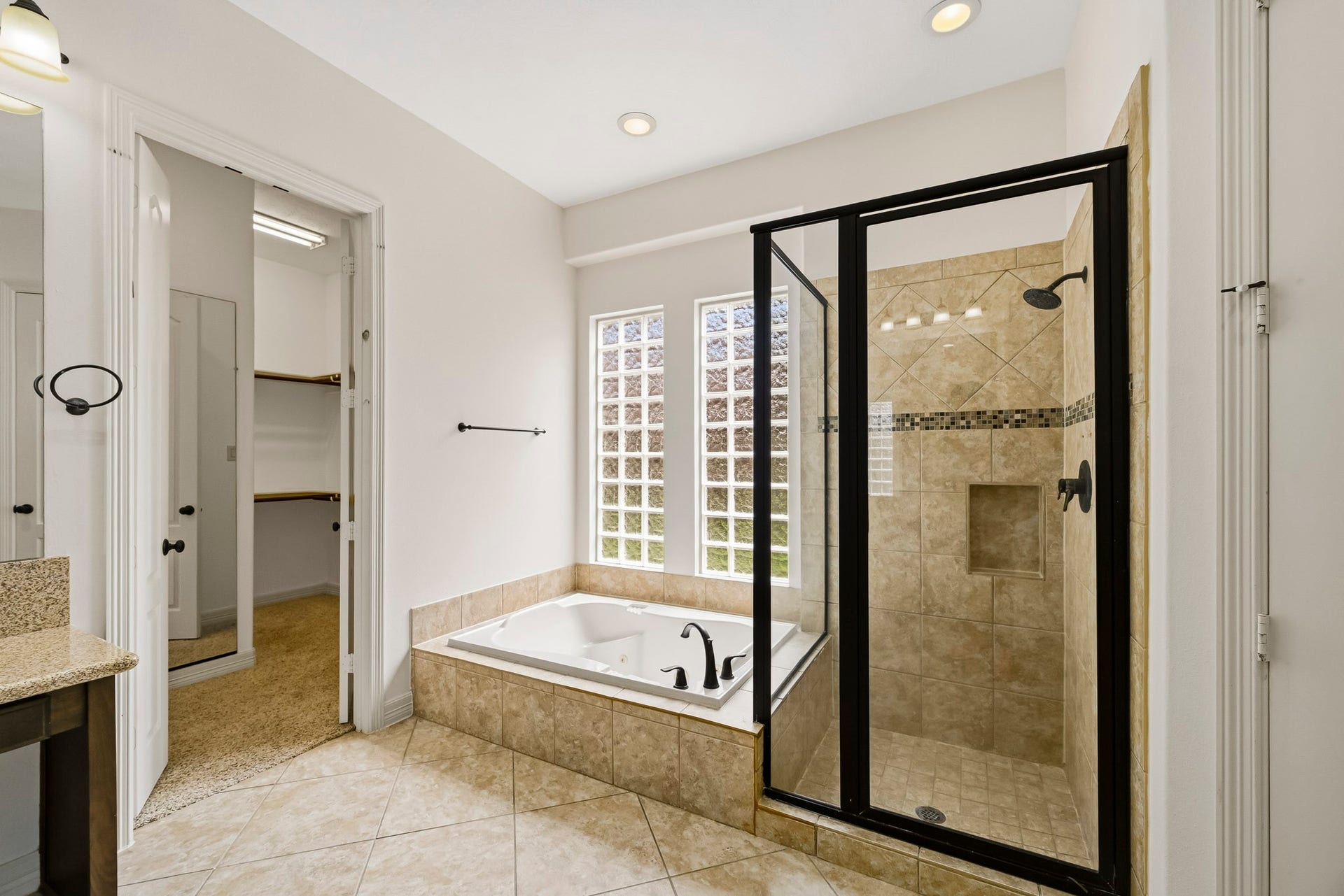 27730 Dalton Bluff Court, Katy, TX 77494 This spacious primary bathroom features a large soaking tub framed by glass-block windows and a separate walk-in shower with tiled walls, decorative accents, a built-in niche, and glass enclosure. Neutral tile flooring, recessed lighting, and dark fixtures create a cohesive look, while direct access to the walk-in closet adds everyday convenience.