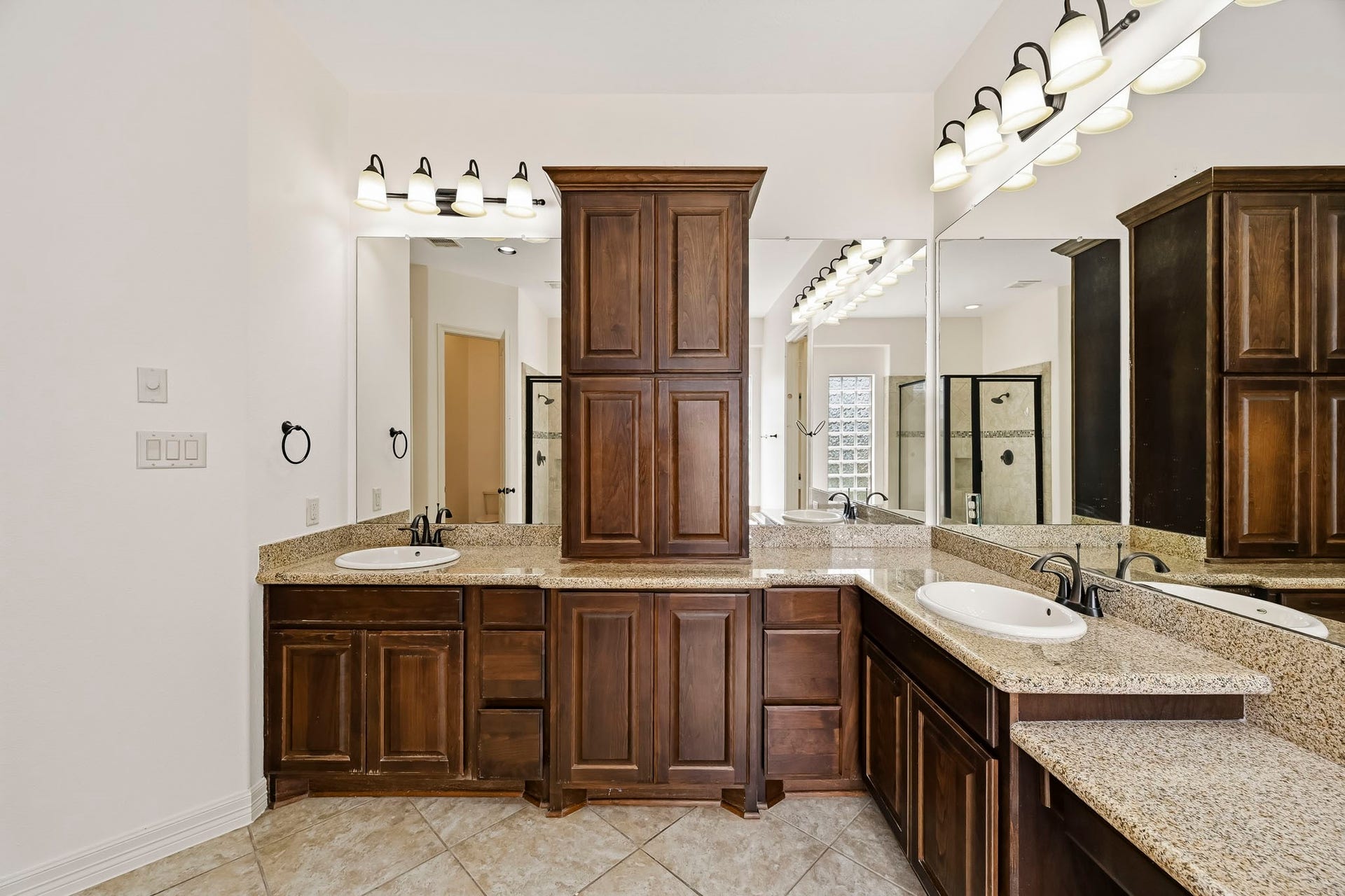 27730 Dalton Bluff Court, Katy, TX 77494 This spacious primary bathroom features an expansive dual-sink vanity with granite countertops, rich wood cabinetry, and abundant built-in storage. Large wall-to-wall mirrors and multiple vanity lights create a bright, open feel, while the extended counter space provides plenty of room for everyday use. Neutral tile flooring complements the warm cabinetry.