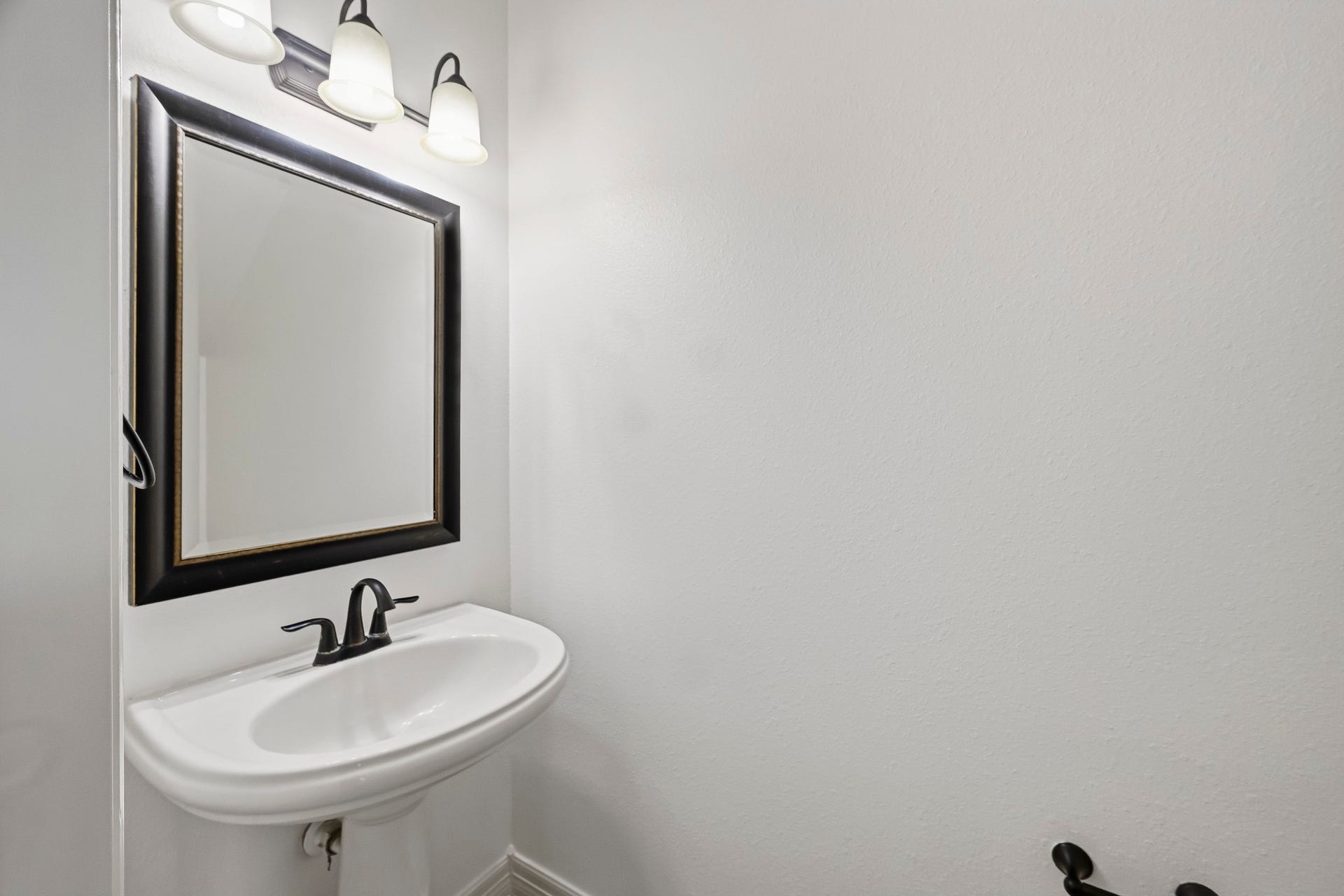27730 Dalton Bluff Court, Katy, TX 77494 This clean half bath features a classic pedestal sink with dark bronze fixtures, a coordinating framed mirror, and a three-light vanity fixture.