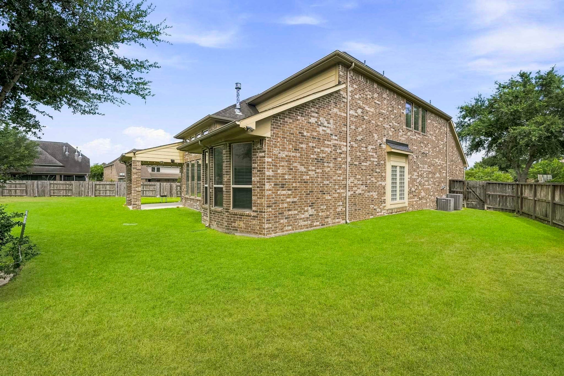 27730 Dalton Bluff Court, Katy, TX 77494 The homes brick exterior, numerous windows, and covered patio overlook the fully fenced yard, while mature trees provide additional greenery and a welcoming outdoor setting.