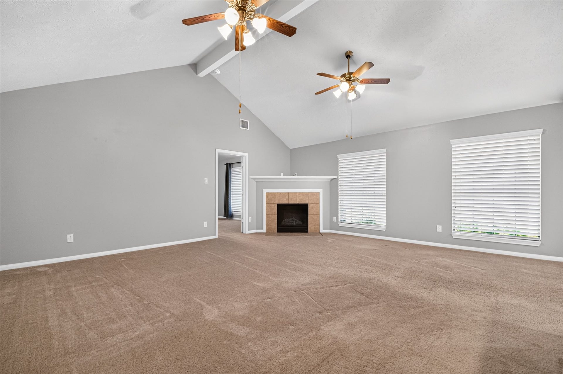 Living room features a high vaulted ceiling, two ceiling fans, a tile-surround fireplace, and windows that bring in natural light.