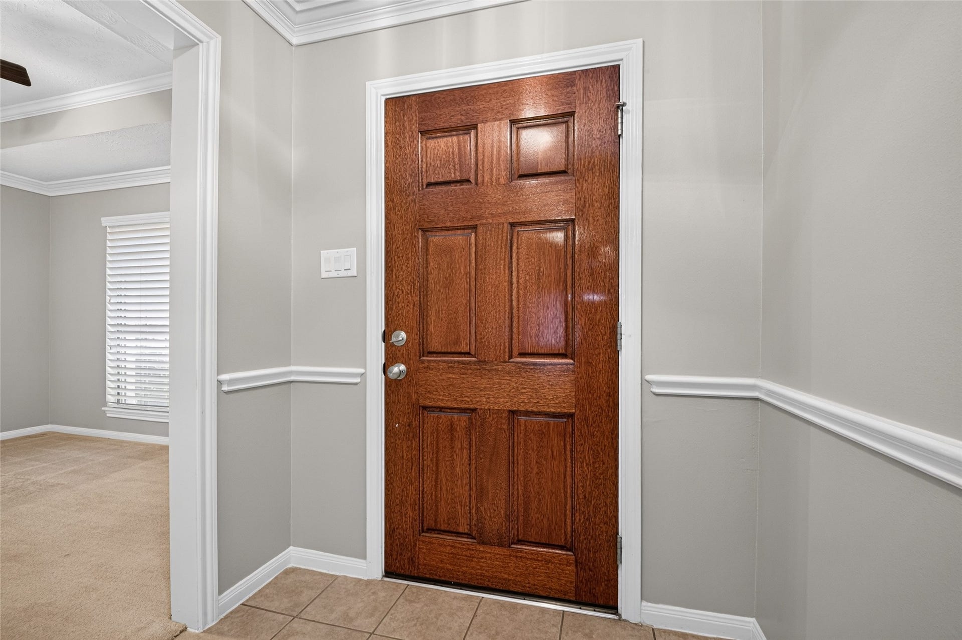 Paneled wood front door opens to an entry with neutral walls, white trim, chair rail detailing, and views into adjoining rooms.