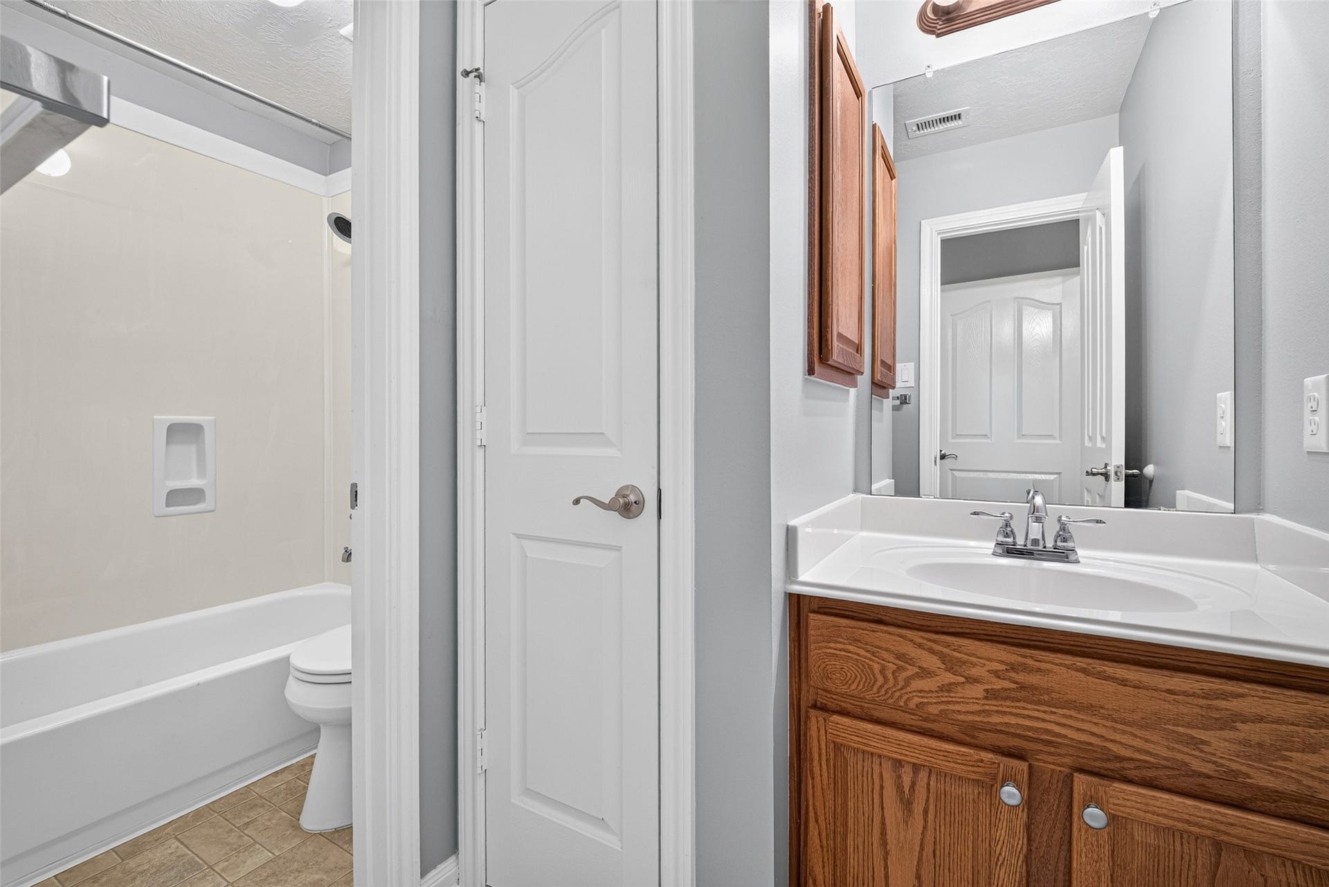 Secondary bathroom features a wood vanity with cabinet storage, and mirrored sink area.