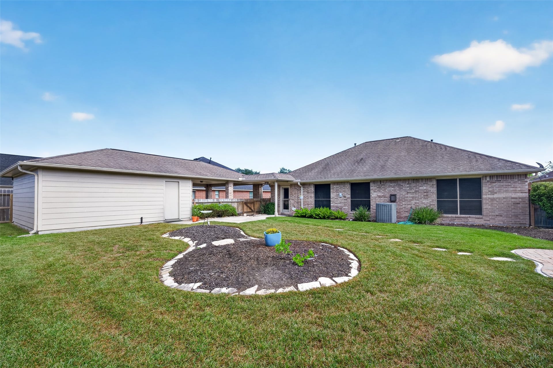 Broad backyard view features a central landscaped bed with stone edging, open lawn, wood fencing, and the detached garage.