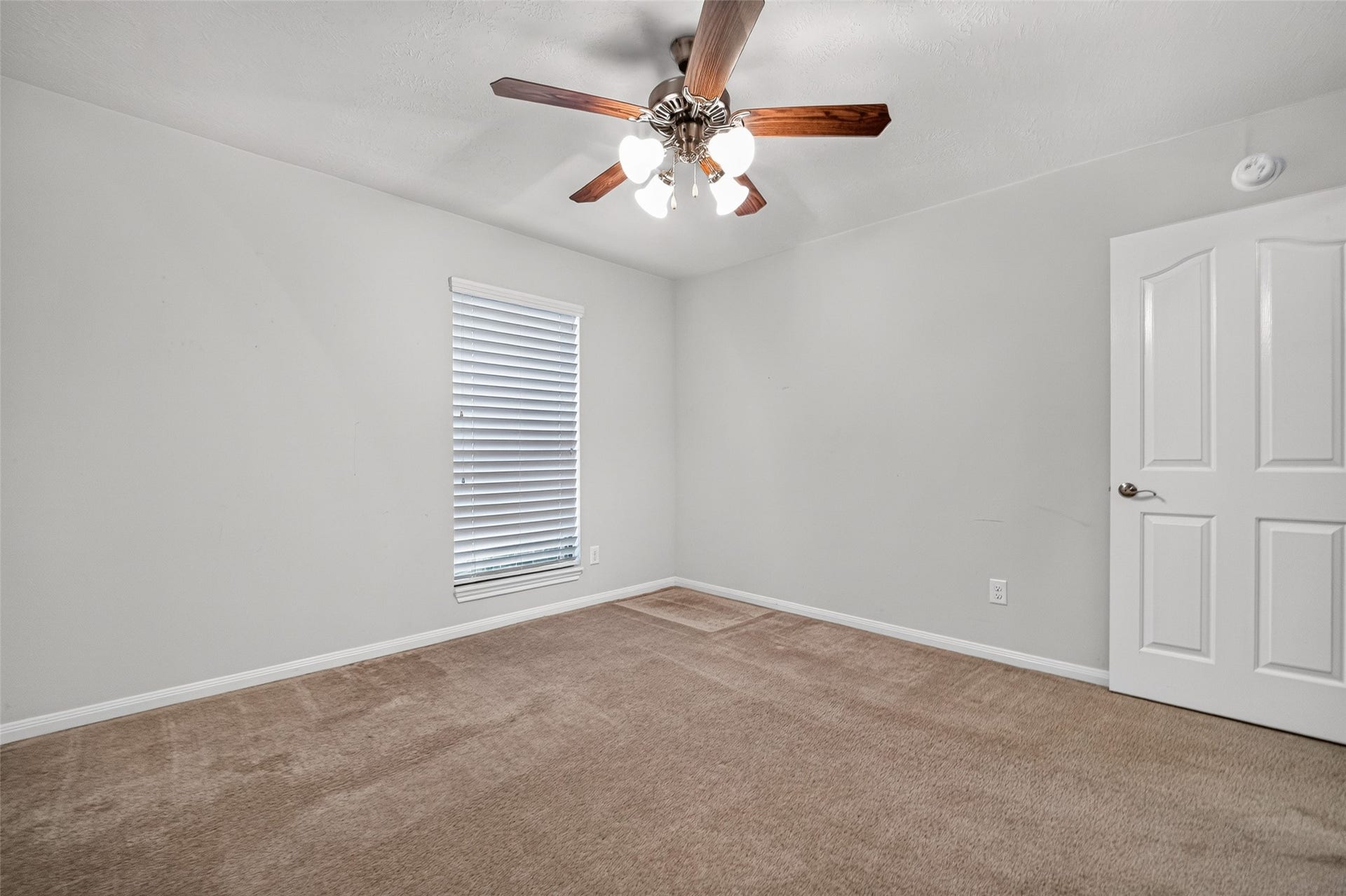 Alternate view of bedroom three highlights the window, ceiling fan, and open floor area beside the paneled entry door.