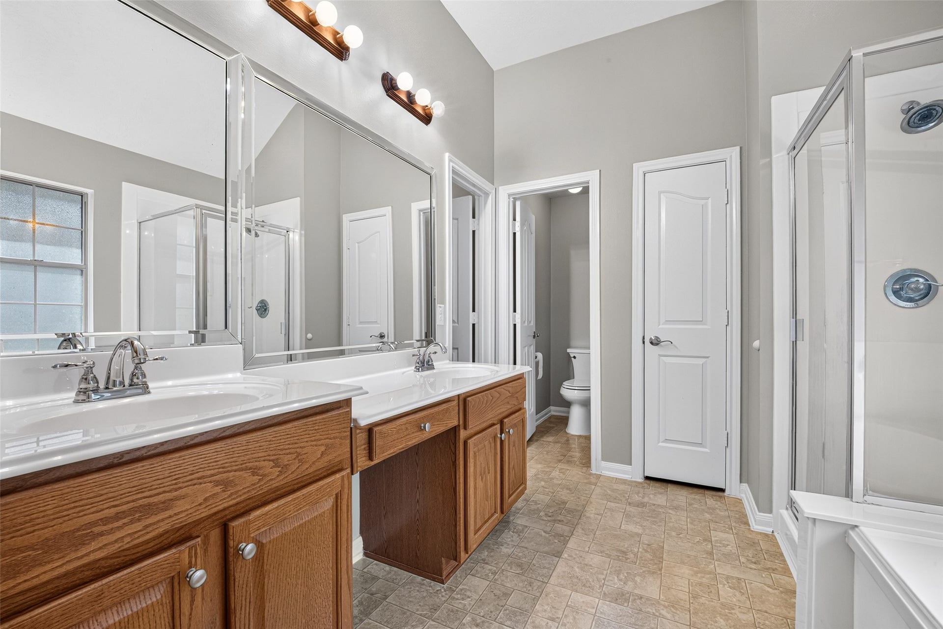 Primary bathroom features a dual-sink vanity, wood cabinetry, broad mirrors, a seated vanity area, and a separate glass-enclosed shower.