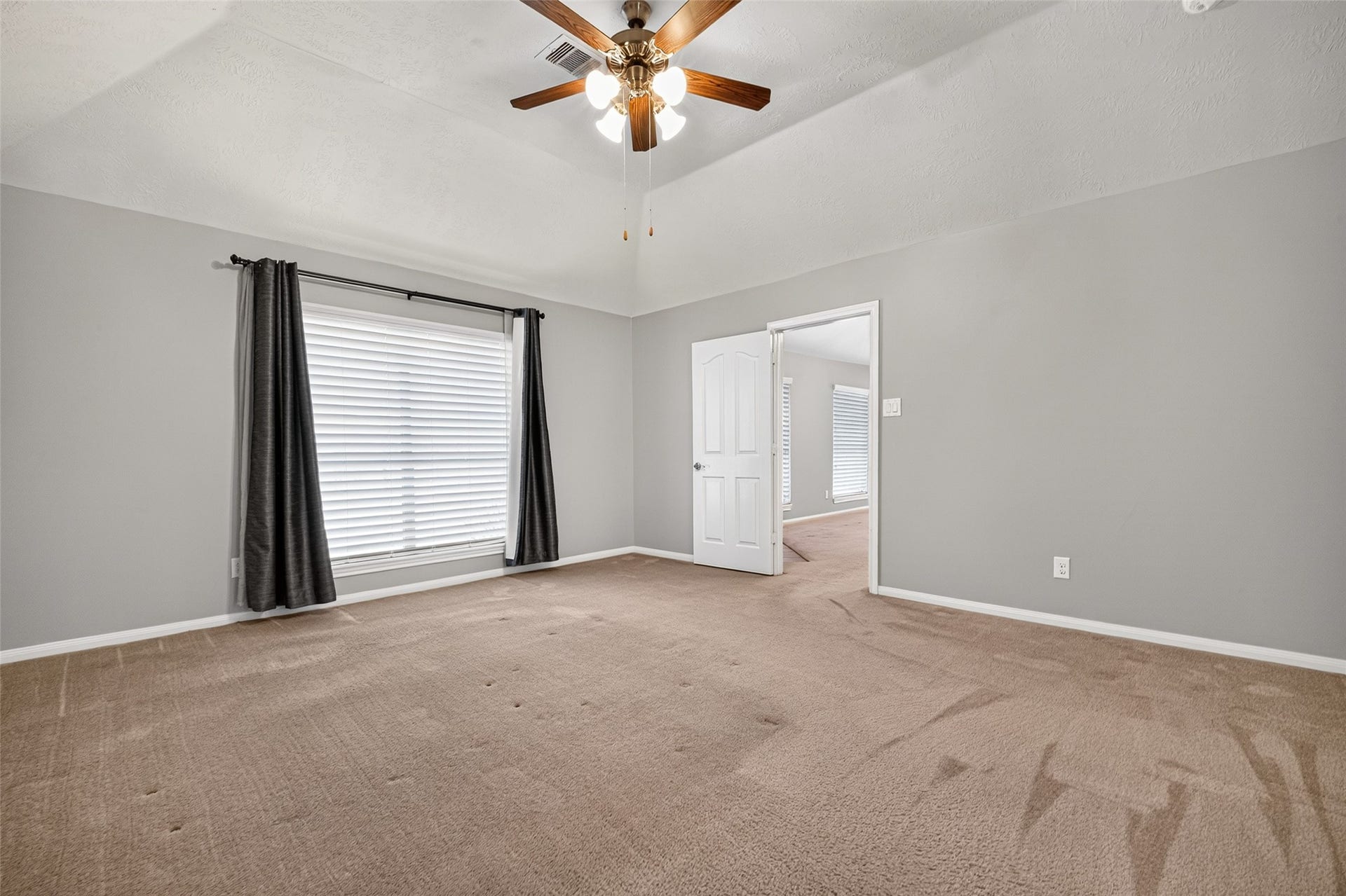 Primary bedroom features a vaulted ceiling, ceiling fan, carpeted flooring, and a large window with white blinds.
