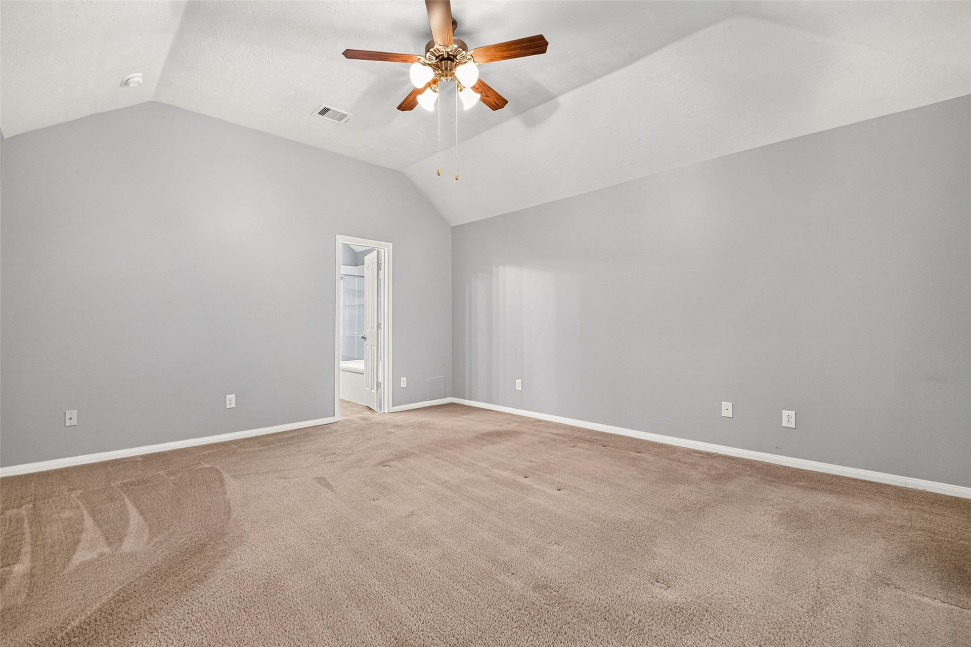 Additional primary-bedroom view showcases neutral walls, white baseboards, carpeted flooring, and the doorway to the adjoining bathroom.
