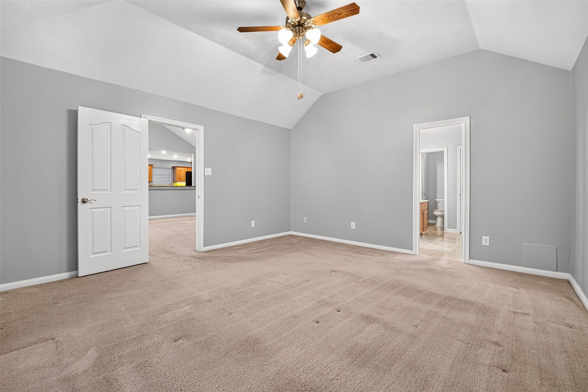 Primary bedroom features a vaulted ceiling, ceiling fan, carpeted flooring, and a large window with white blinds.
