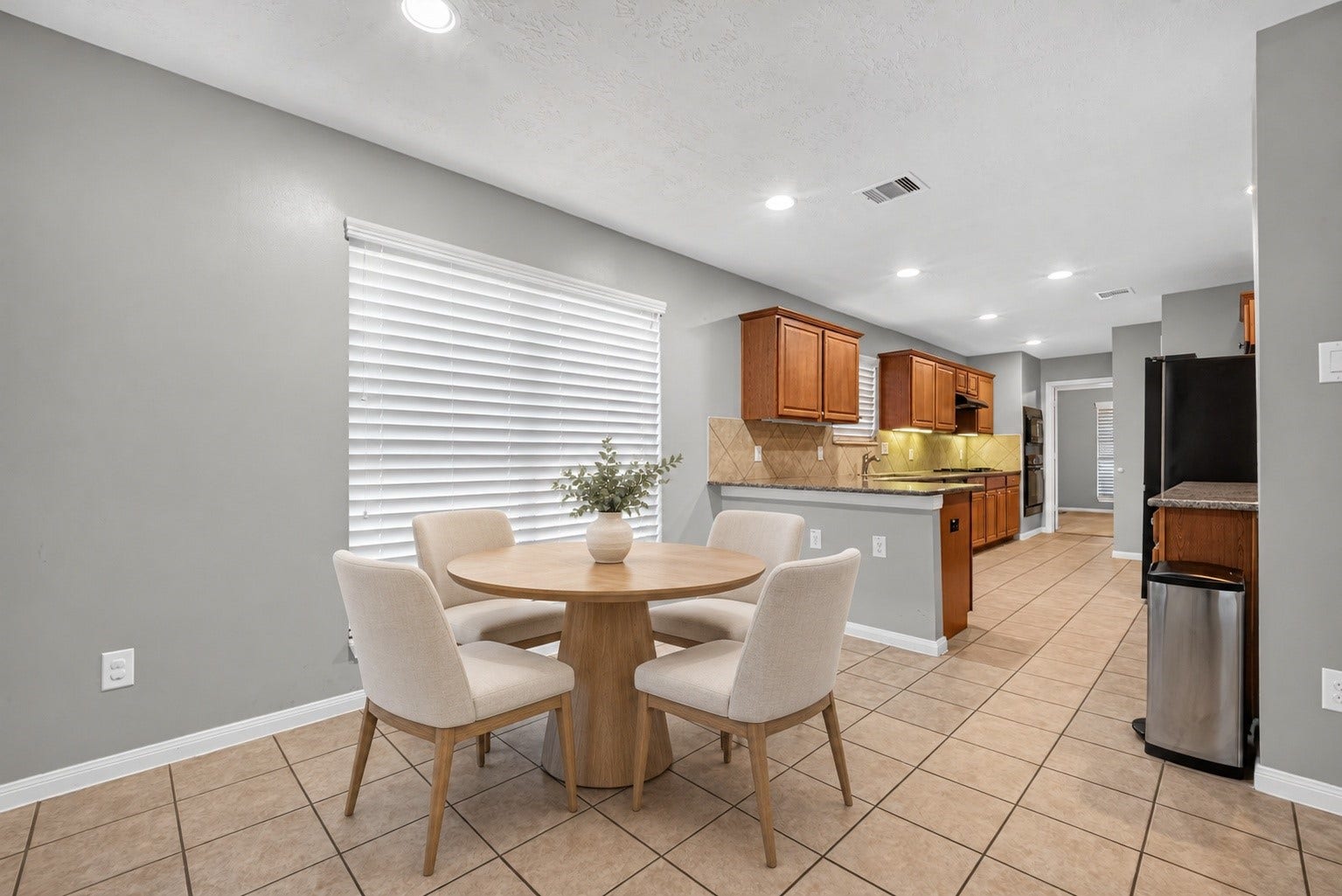Virtually staged breakfast area showcases space for a dining table beside the large window, with tile flooring and direct access to the kitchen.
