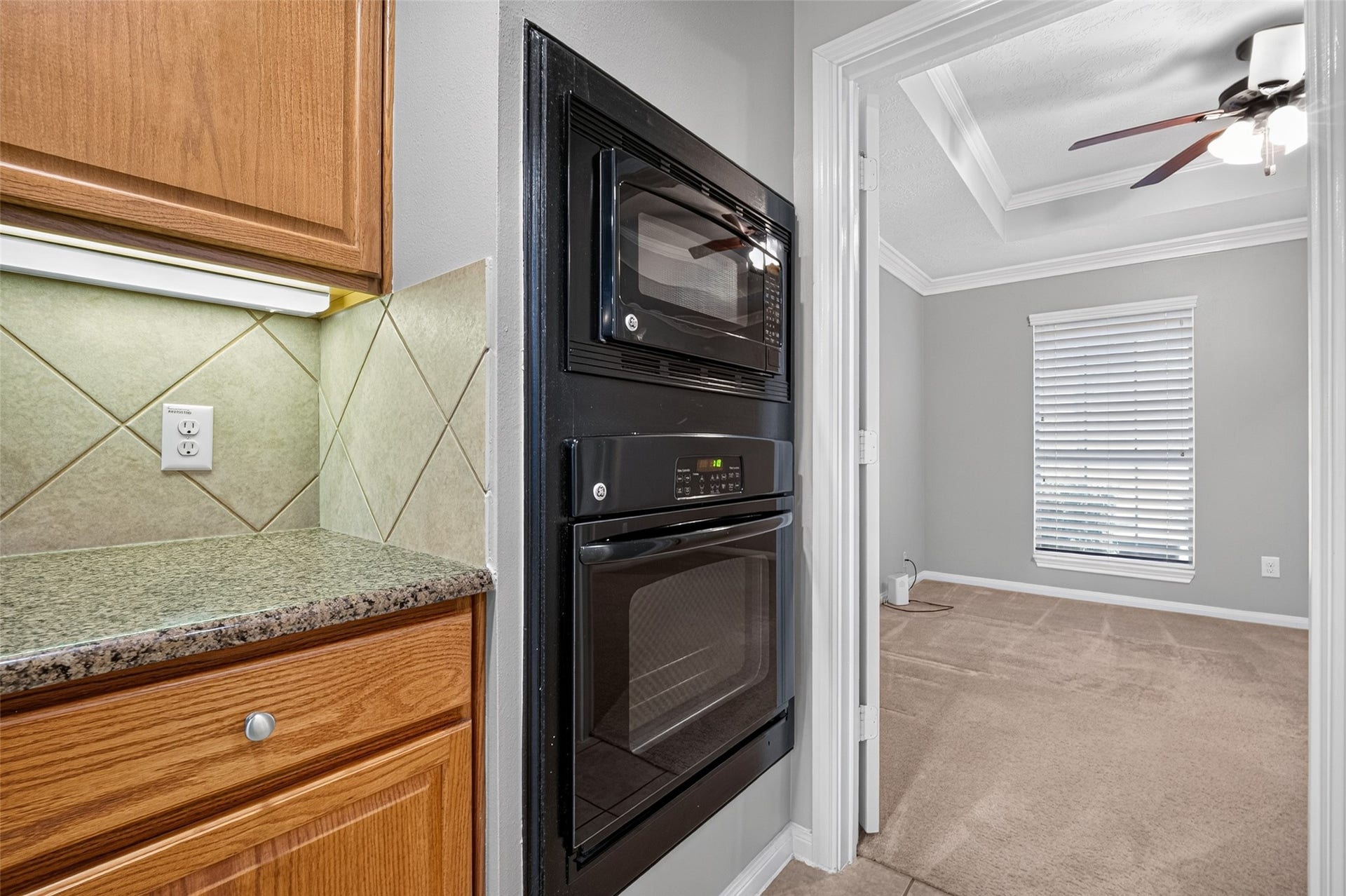 Built-in microwave and wall oven are positioned beside a granite-look counter, wood cabinetry, and a diagonally patterned tile backsplash.