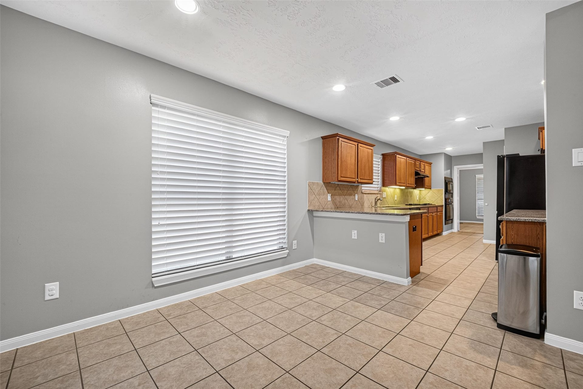Breakfast area offers tile flooring, a large window with white blinds, and an open connection to the kitchen and counter.