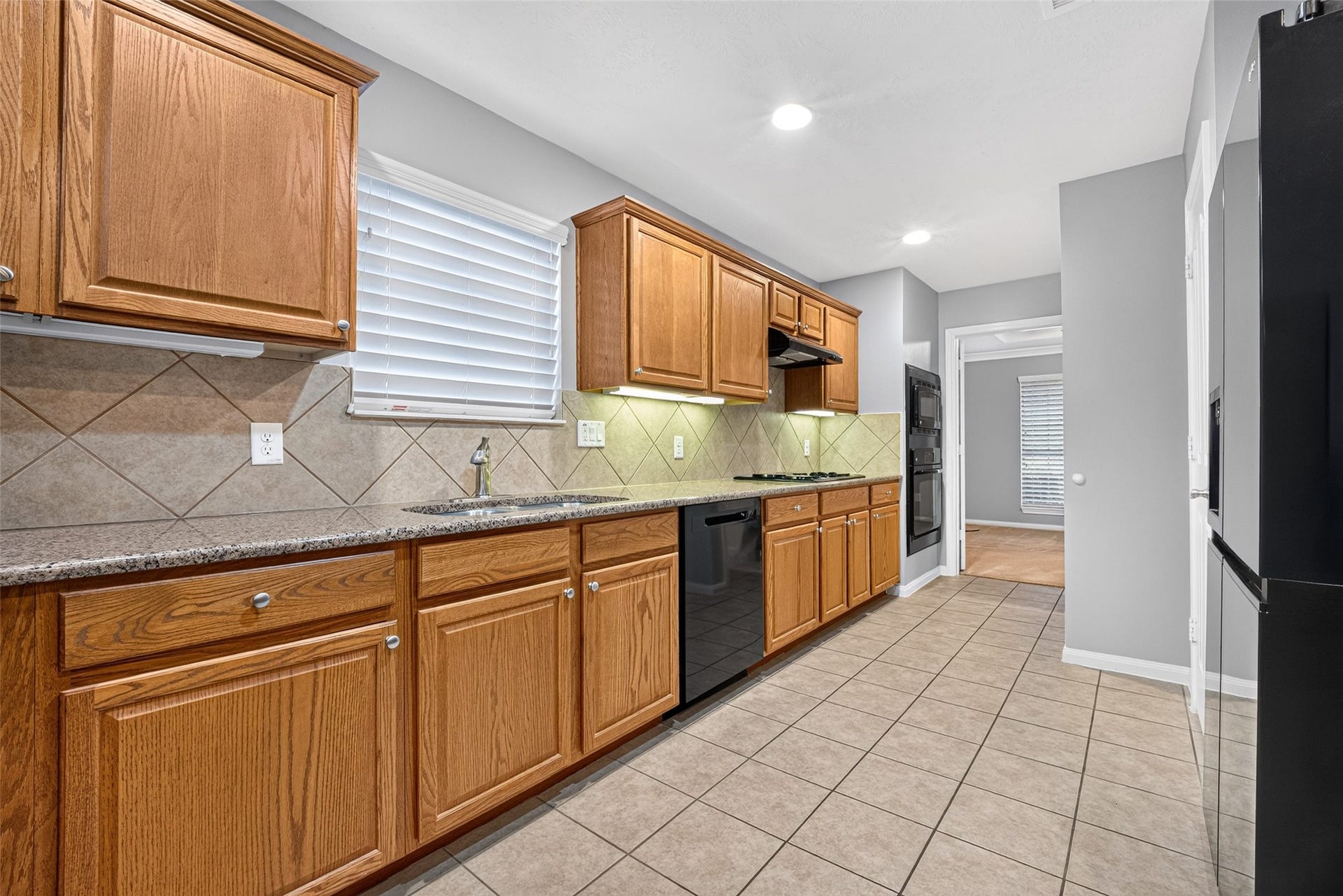 Sink-side kitchen view showcases a window above the sink, black dishwasher, wood cabinetry, and continuous counter space beneath recessed lighting.