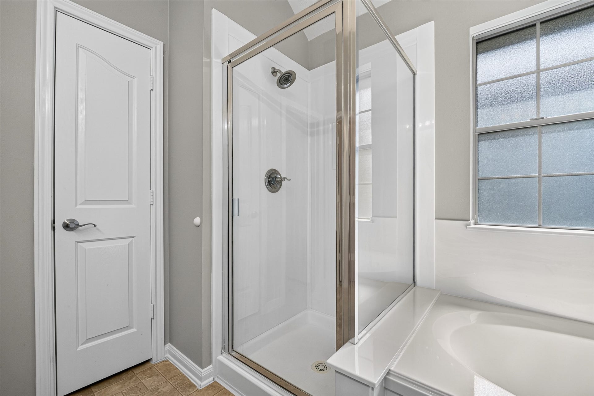 Closer view of the primary bathing area highlights the separate shower enclosure, adjacent tub, and window above the tub surround.