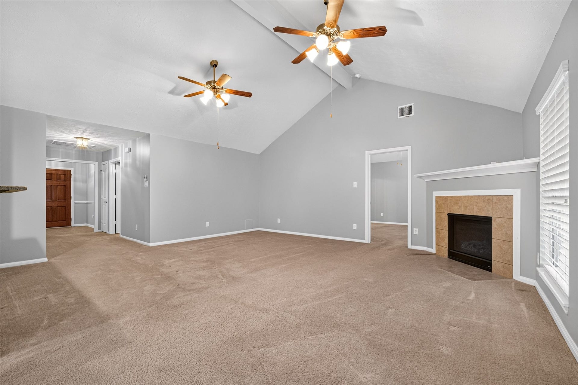 Wide living-room view highlights the vaulted ceiling, fireplace with white mantel, neutral carpet, and access to adjoining areas.