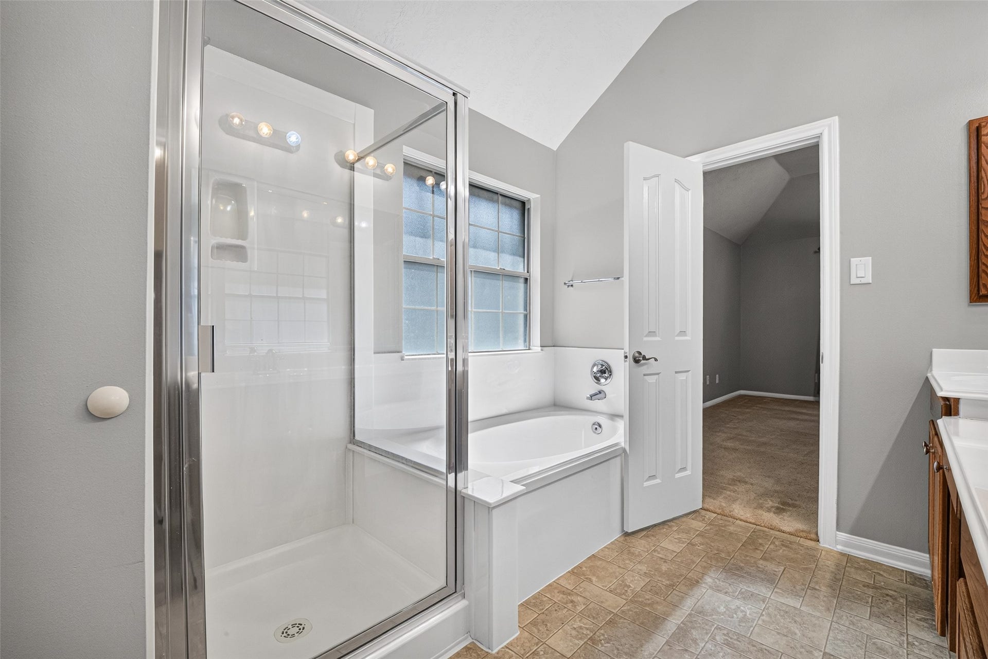 Primary bathroom offers a separate glass-enclosed shower and soaking tub beneath a window, with tile flooring throughout the bathing area.