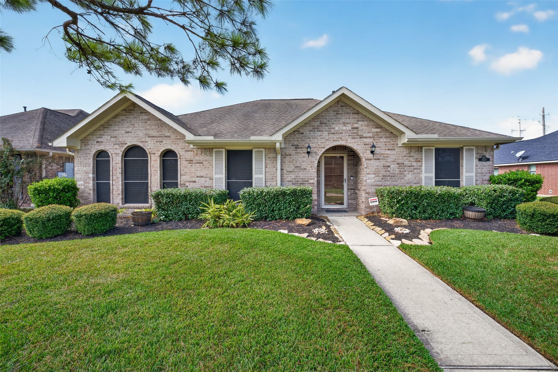 Front elevation showcases the brick exterior, arched windows, recessed arched entry, and landscaped beds bordering the front walkway.