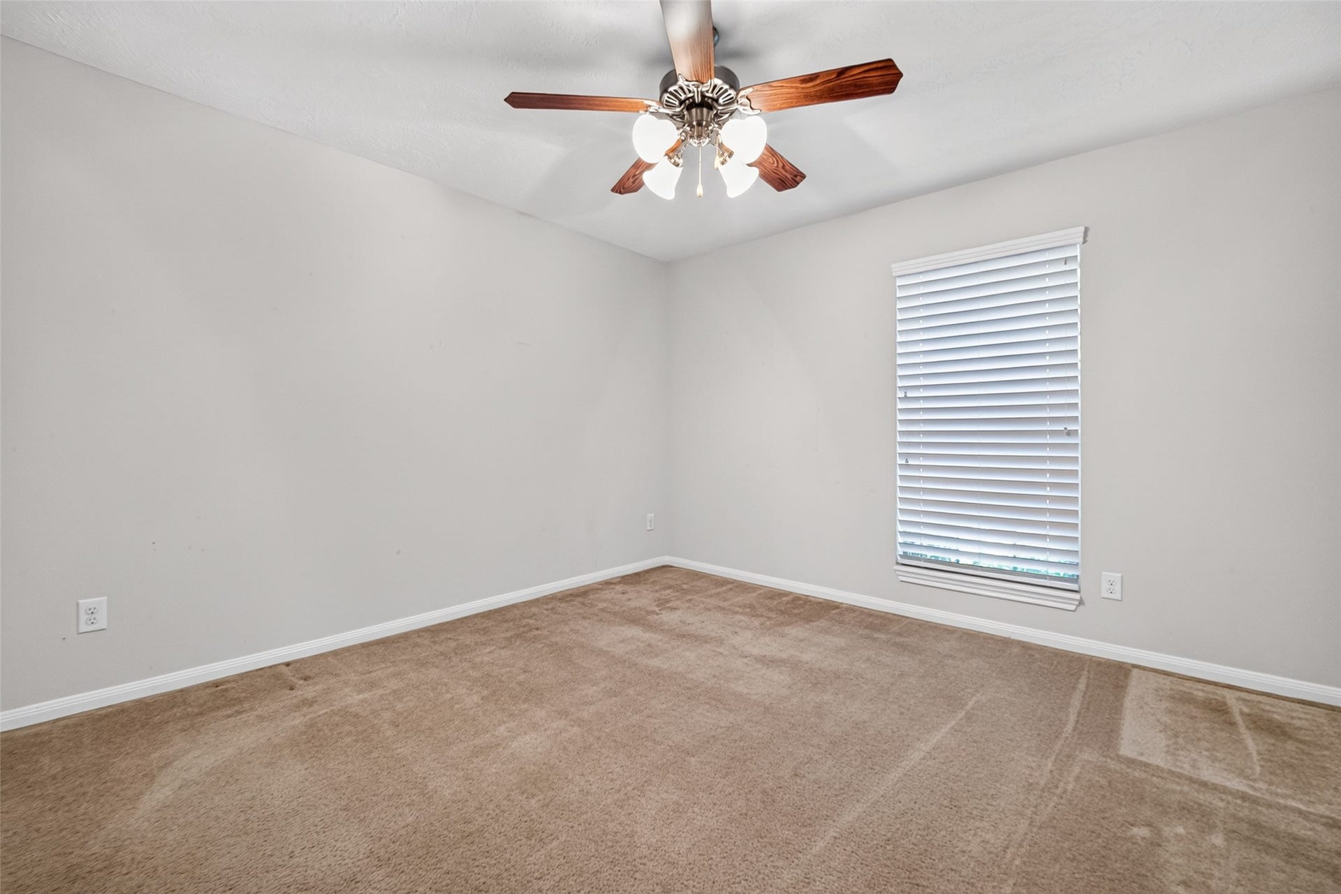 Bedroom three offers carpeted flooring, neutral walls, a ceiling fan with lighting, and a window with white blinds.