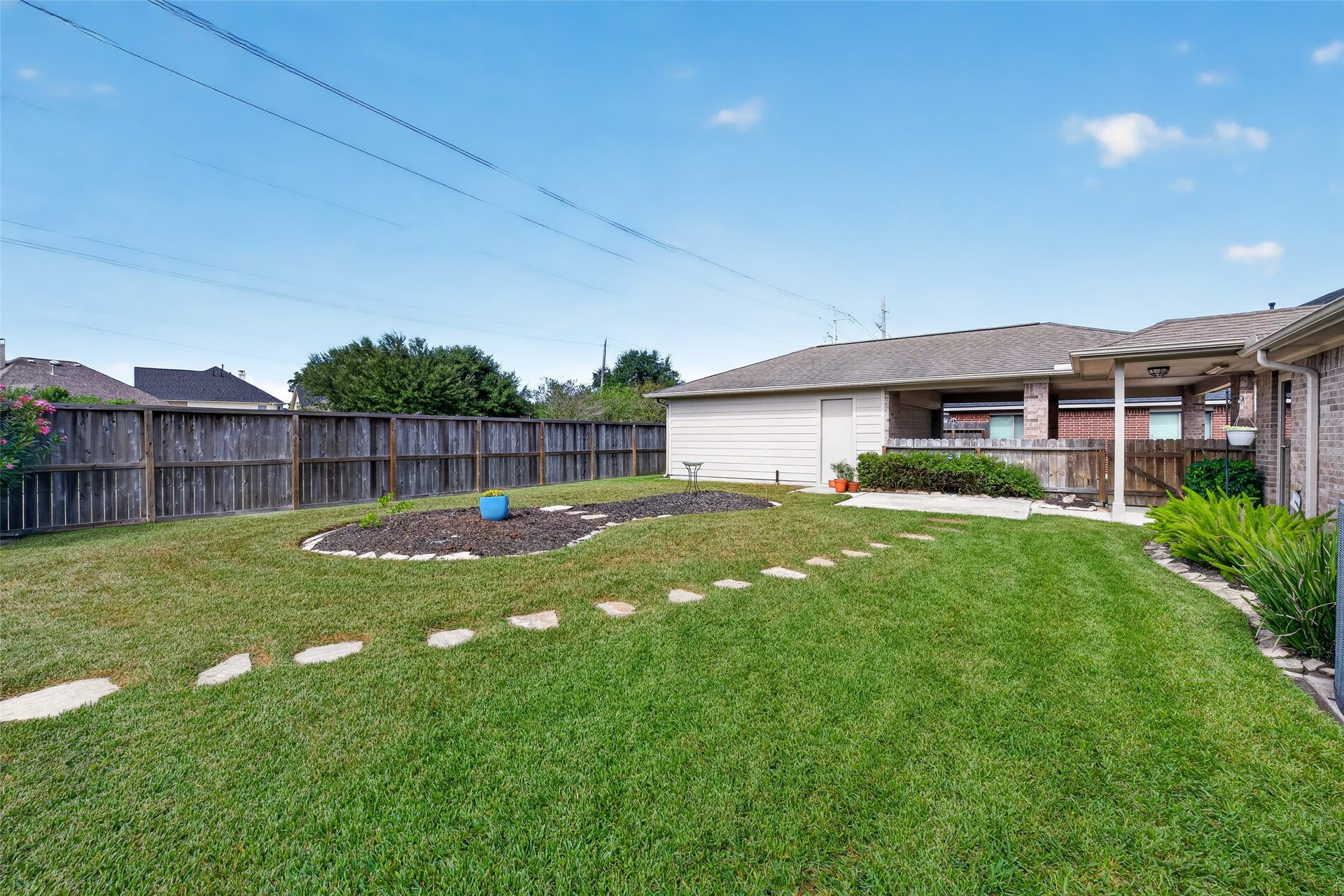 Backyard view showcases an open lawn, curved stepping-stone path, landscaped island bed, and detached garage along the rear boundary.