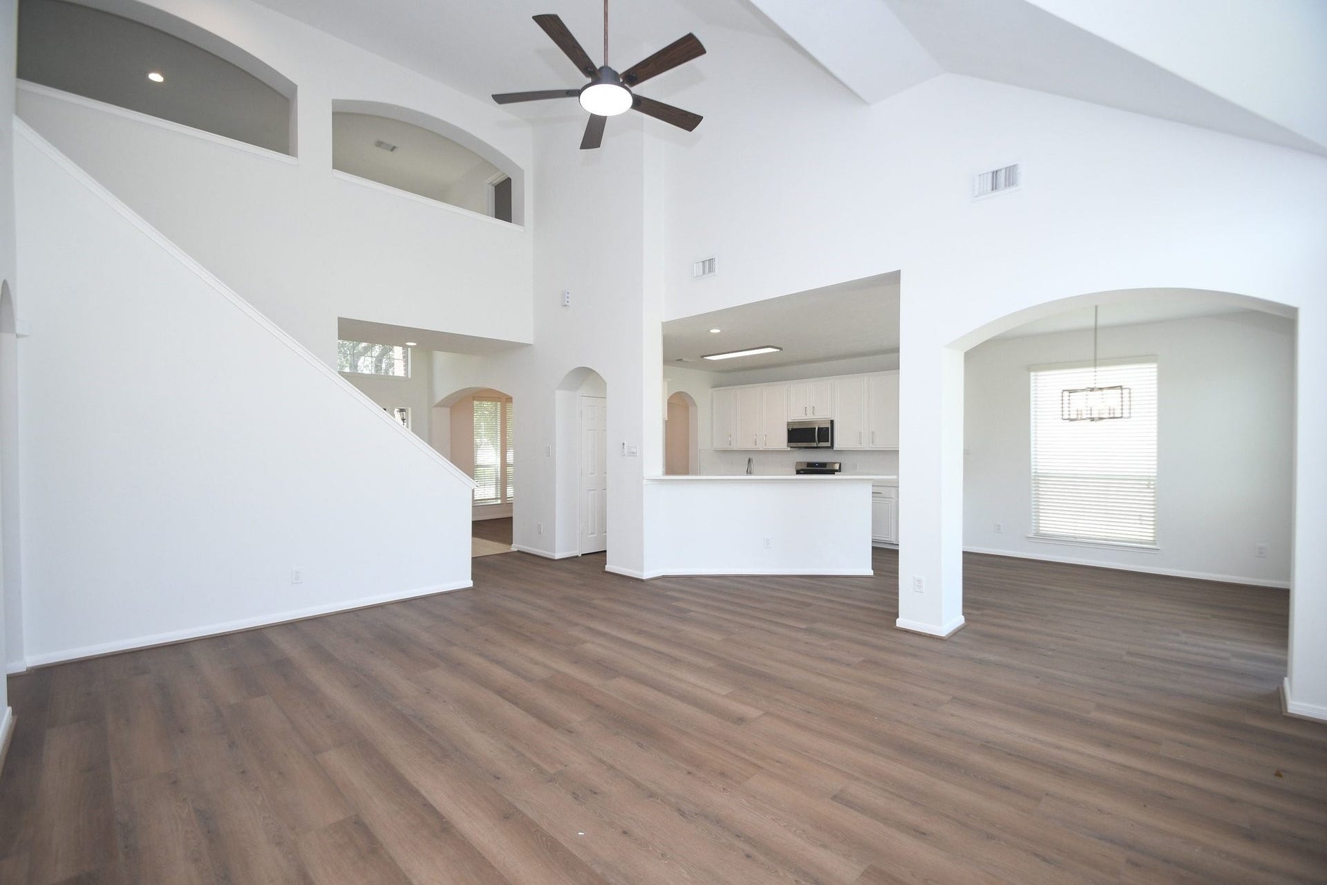 9111 Morningstar Drive, Sugar Land, TX 77479 Spacious open-concept living area with high ceilings, elegant wood flooring, and abundant natural light, seamlessly connected to a modern kitchen with white cabinetry and stainless steel appliances.