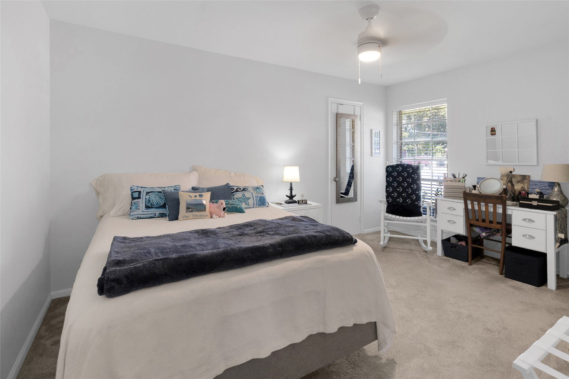 613 N Avenue F, Humble, TX 77338 Second bedroom with soft carpeting, a comfortable bed adorned with decorative pillows, and ample natural light from a large window. A ceiling fan and a workspace add functionality, while neutral tones create a serene atmosphere.