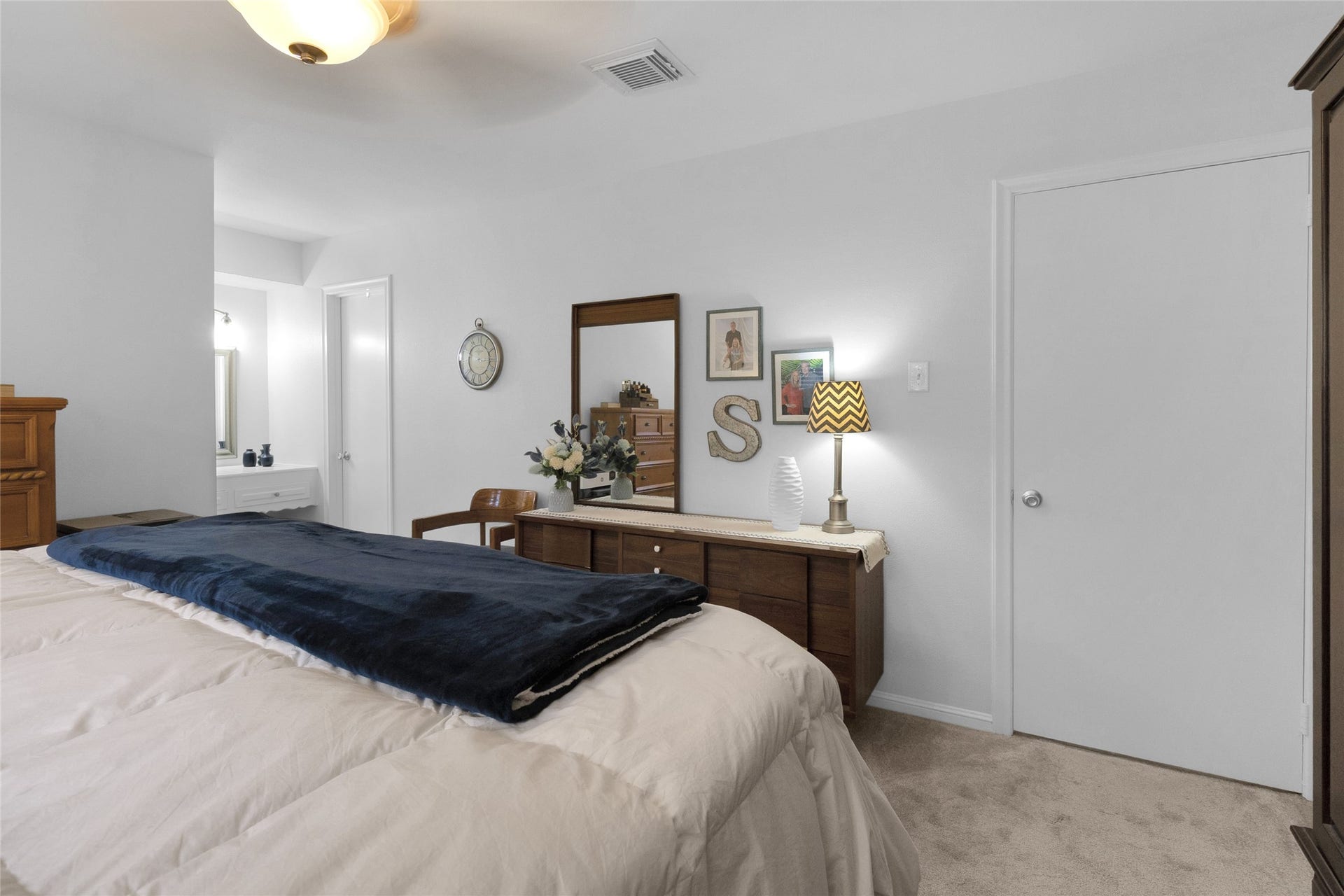 613 N Avenue F, Humble, TX 77338 Spacious bedroom with modern decor, featuring a cozy bed, elegant dresser, and convenient access to a well-lit bathroom.