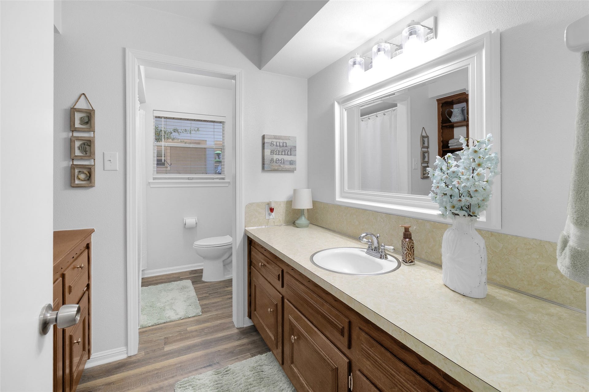 613 N Avenue F, Humble, TX 77338 Charming bathroom with a large mirror, ample countertop space, and warm wood cabinetry. The room is brightened by soft lighting and complemented by tasteful decor, creating a welcoming and functional space.