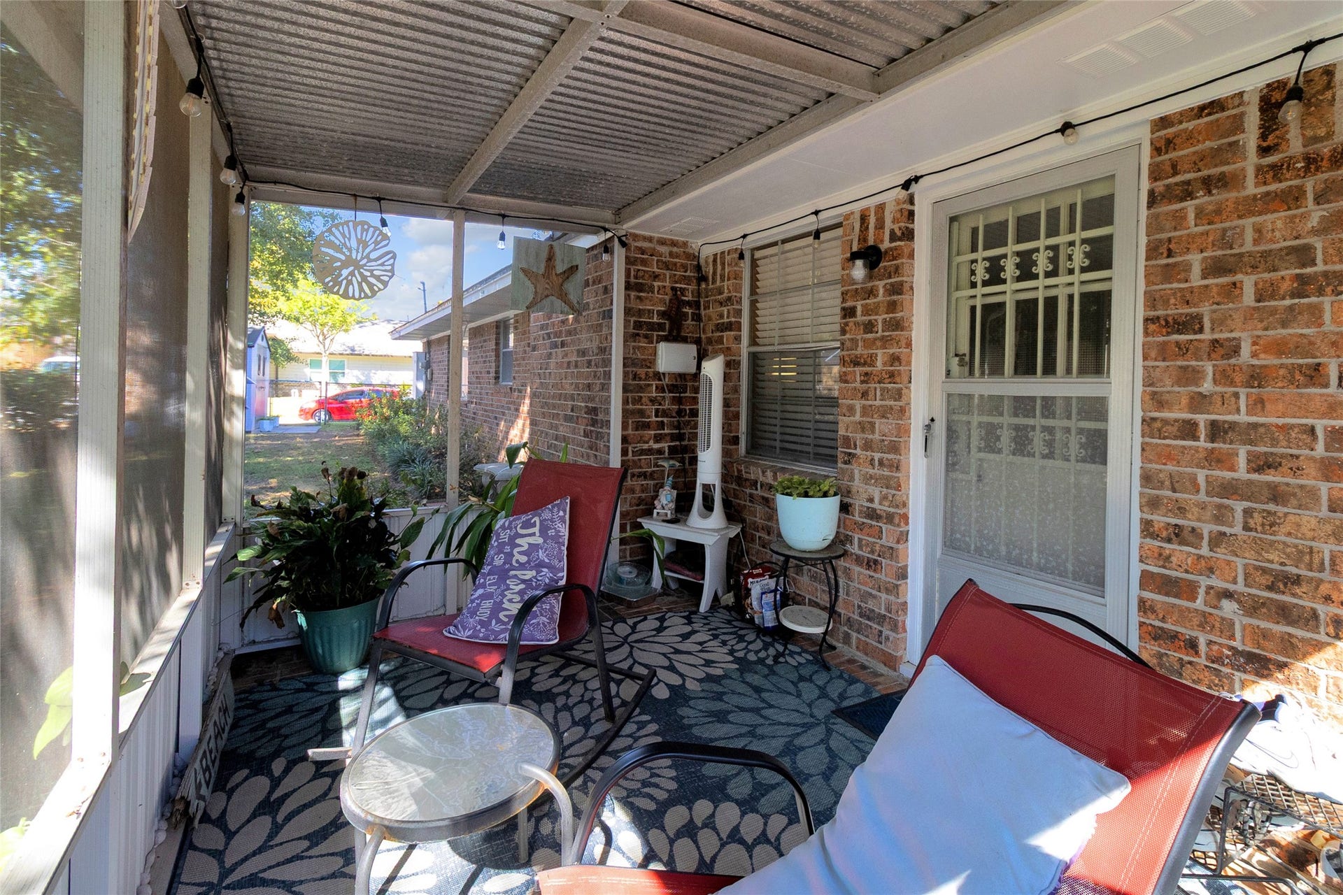 613 N Avenue F, Humble, TX 77338 Charming screened-in porch with cozy seating, vibrant plants, and a decorative rug, perfect for relaxing outdoors.